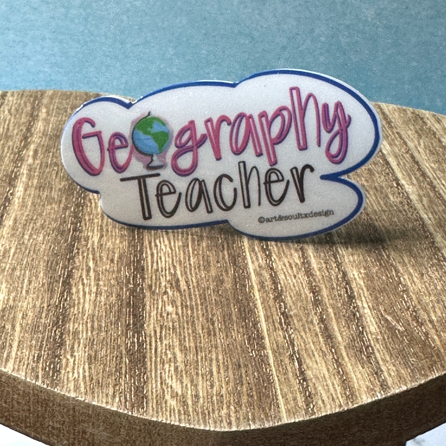Geography Teacher waterproof vinyl sticker standing upright on rustic wooden table surface lifestyle photo.