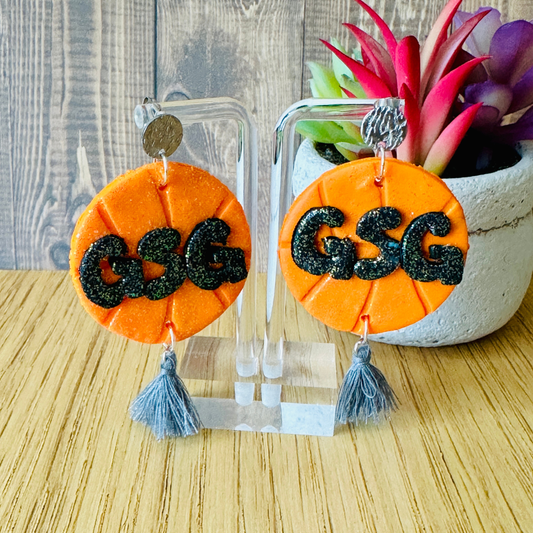 Handmade orange GSG basketball polymer clay earrings with silver tassel on earring stand, wooden table, Texas-made.