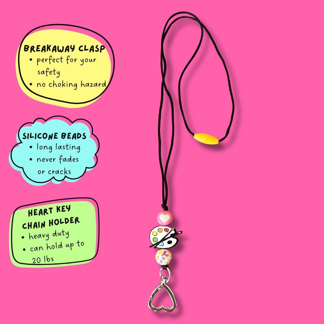 A beaded Paint Palette Lanyard with a heart-shaped key ring holder and a breakaway clasp, displayed on a bright pink background with three colorful text callout boxes describing its features.