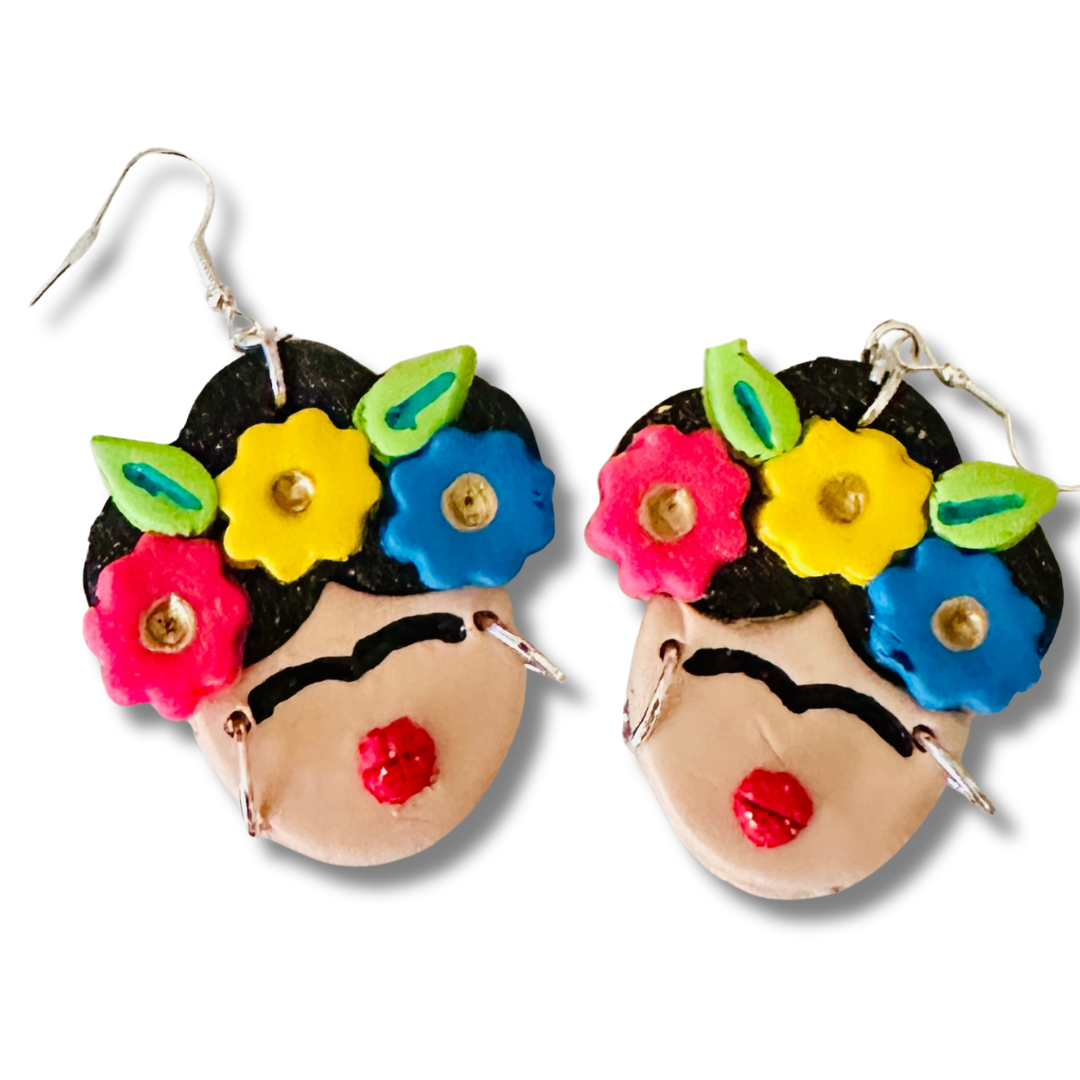 A close-up of the large Frida Kahlo Bold Flower Crown polymer clay earrings.  The larger blue, red, and yellow flowers and bright red lips stand out against the white background.  The silver hoops look like Frida's earrings.
