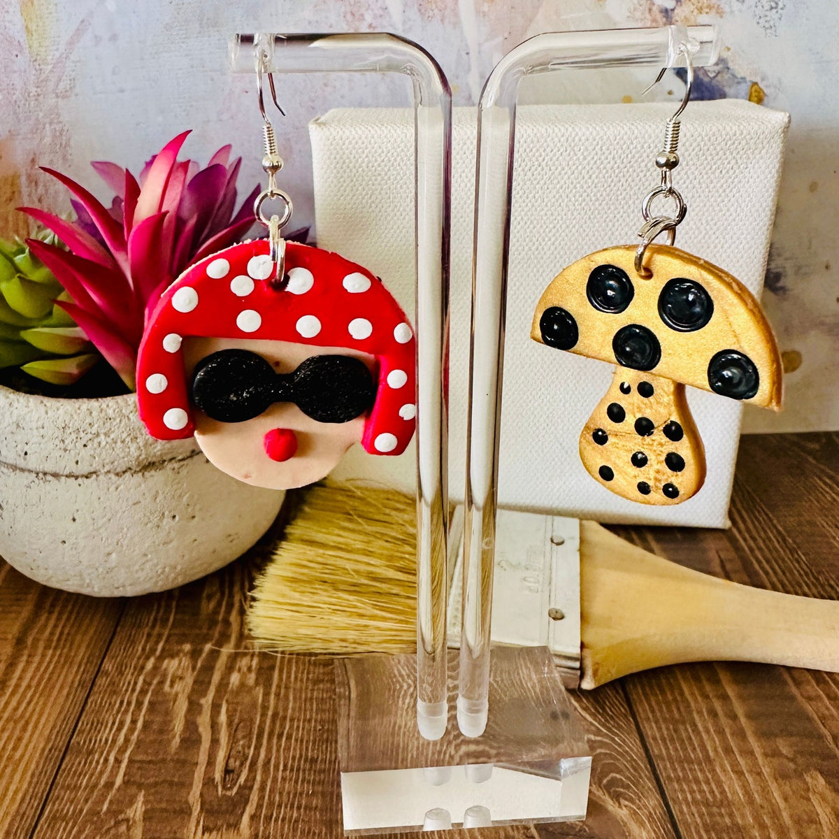 Close-up detail of large Yayoi Kusama polymer clay earrings showing artistic portrait with red polka dot hair, black sunglasses, red lips.
