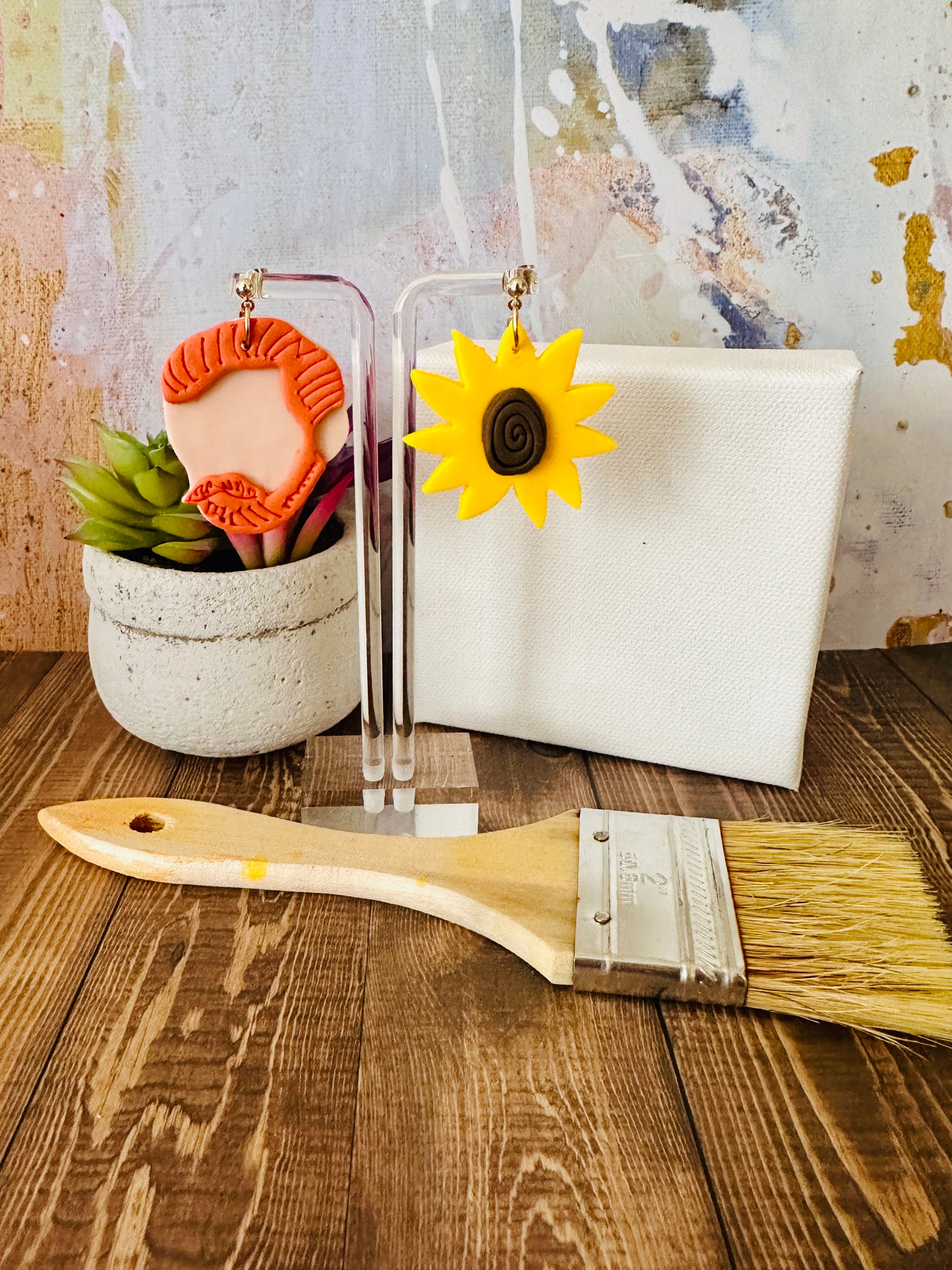 Large Van Gogh art teacher earrings on clear stand with paintbrush, plant on wood table, vibrant abstract wall background.