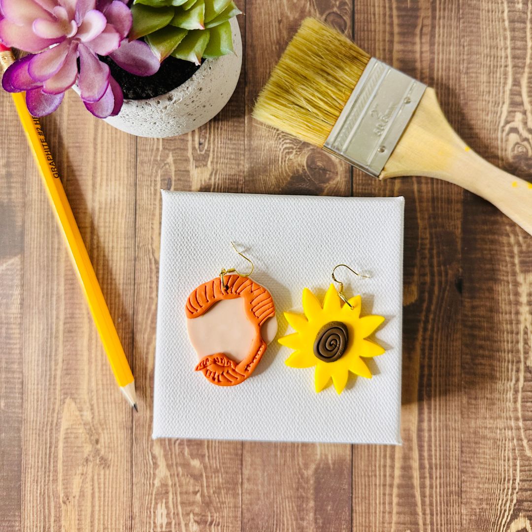 Large Van Gogh portrait and sunflower earrings on white canvas with paintbrush and succulent plant art studio flat lay.