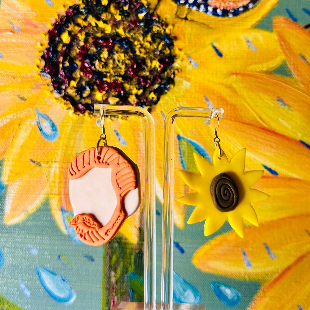 Detailed close up of large Van Gogh earrings showing red hair texture and sunflower swirls with sunflower painting backdrop.