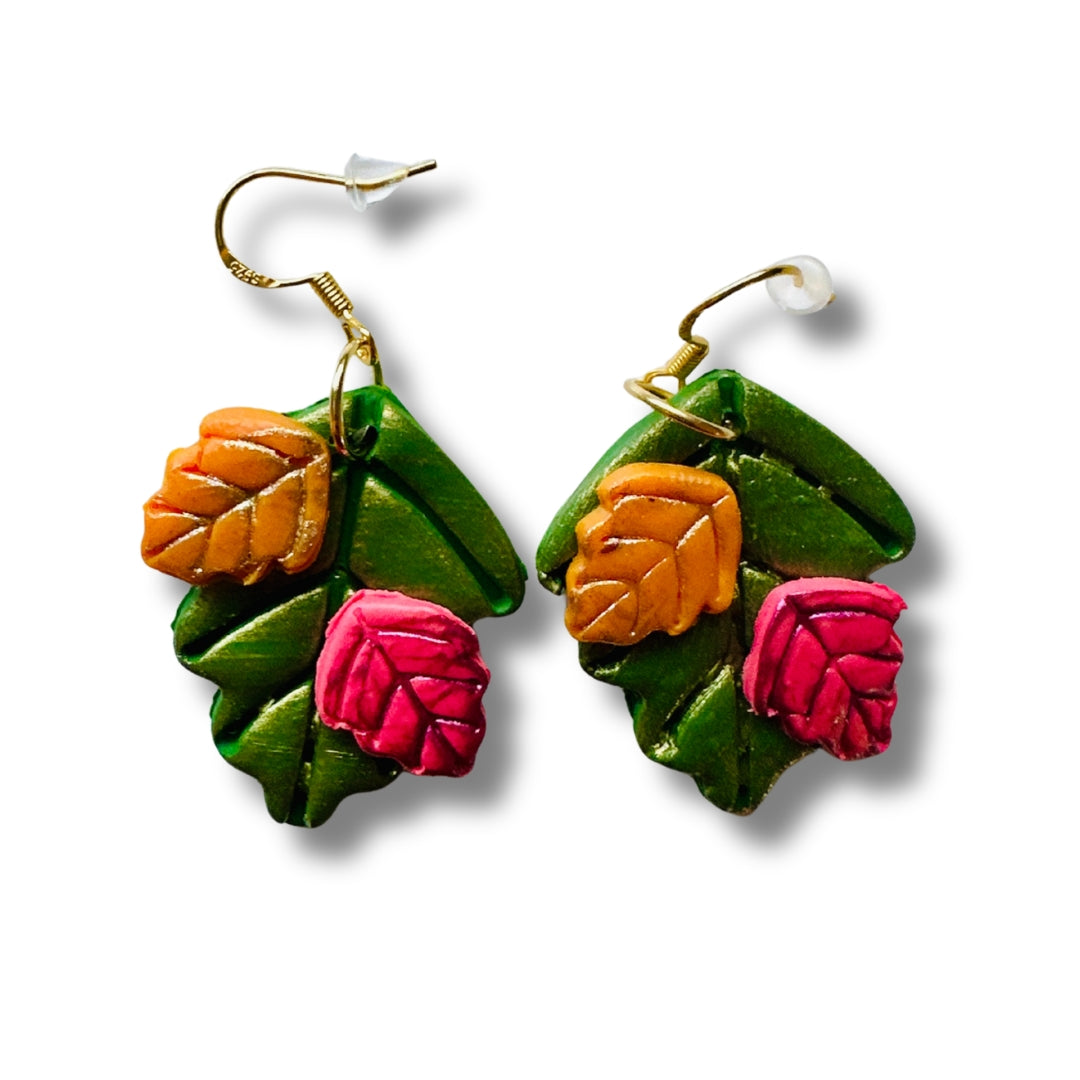 A pair of dangling earrings shaped like autumn leaves, featuring textured forest green leaves with raised pumpkin orange and cranberry leaf details, suspended from gold-tone hooks on a white background.