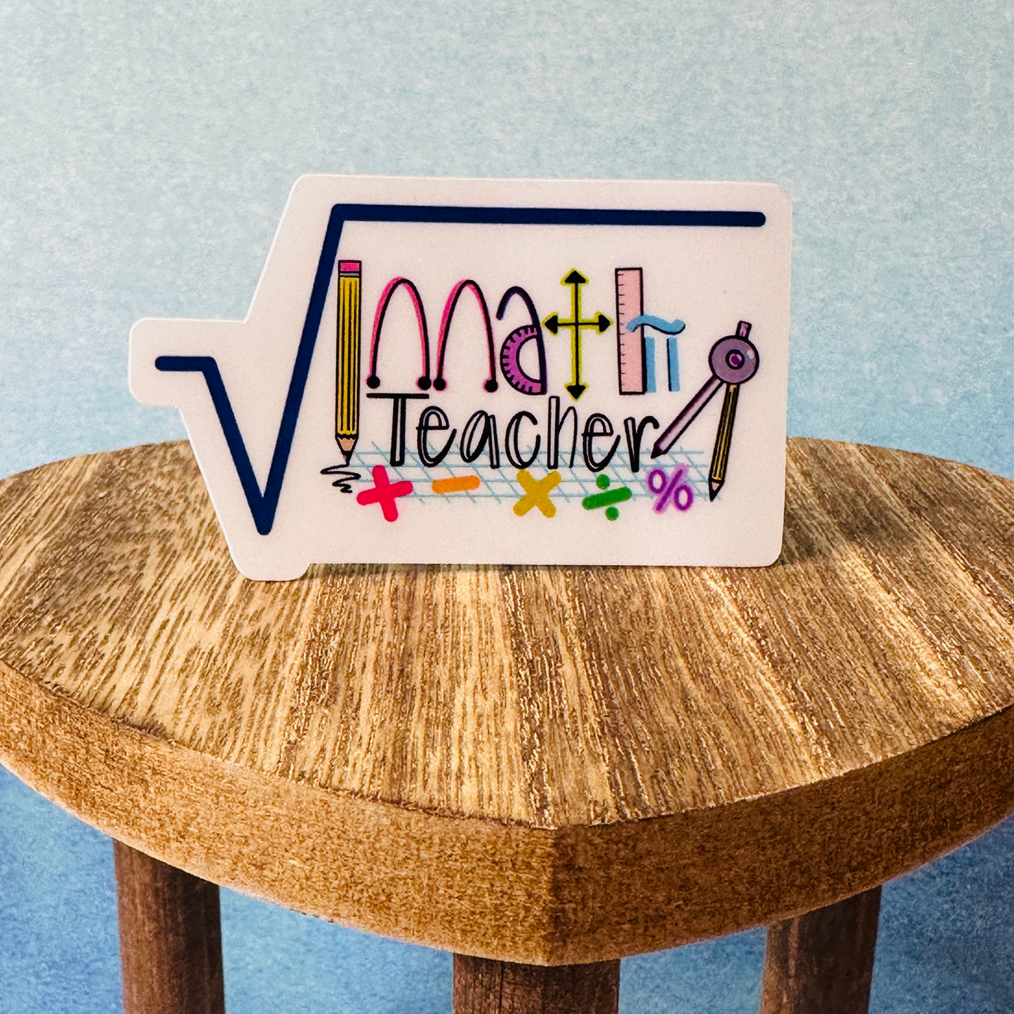 Math teacher weatherproof vinyl sticker standing on wooden table, blue wall background, showing size and design.