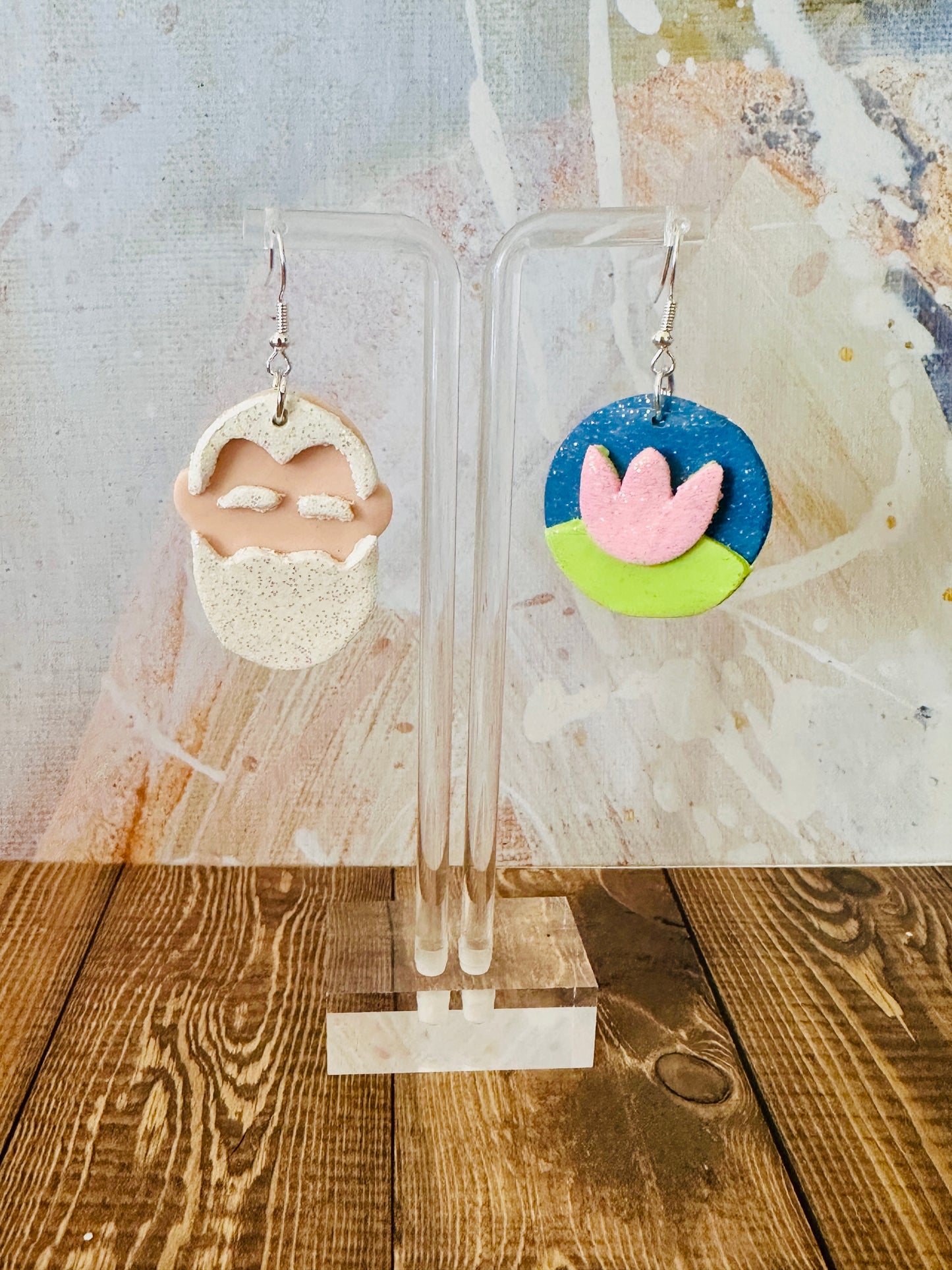 Lightweight polymer clay Claude Monet art teacher earrings hanging on earring stand with colorful abstract wall backdrop.