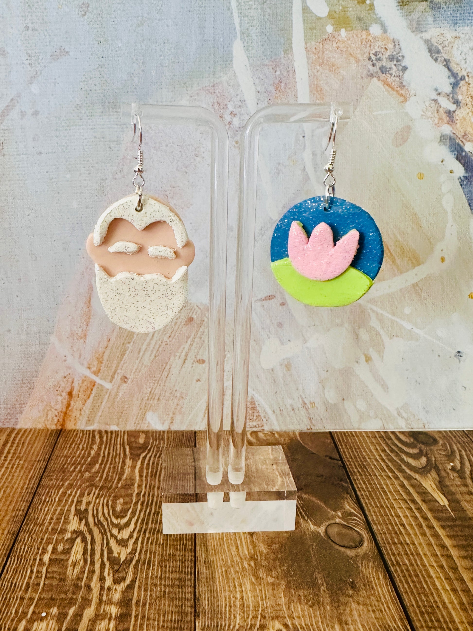 Lightweight polymer clay Claude Monet art teacher earrings hanging on earring stand with colorful abstract wall backdrop.