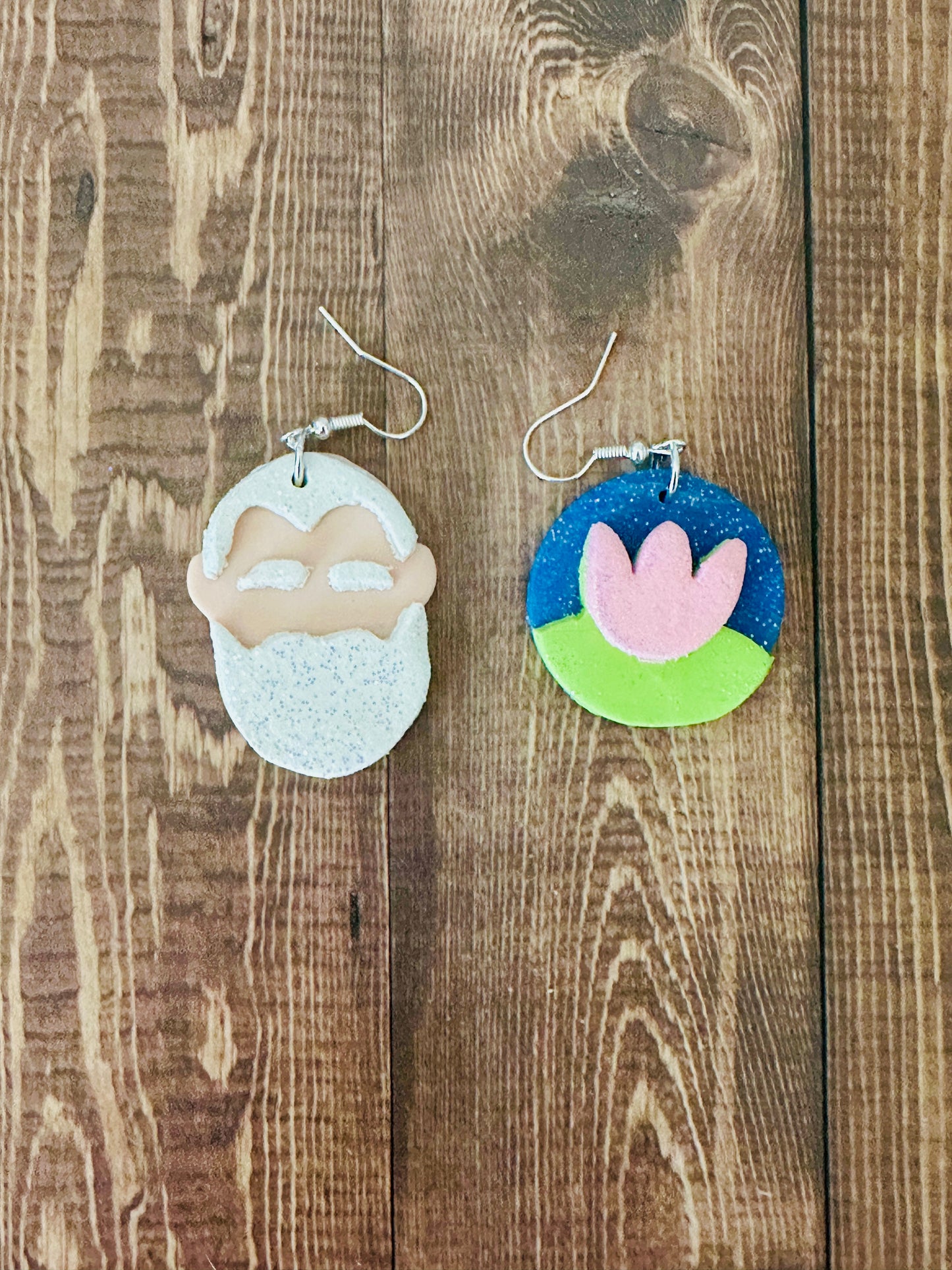 Handcrafted Claude Monet artist earrings with white beard portrait and water lily design on dark wooden table surface.