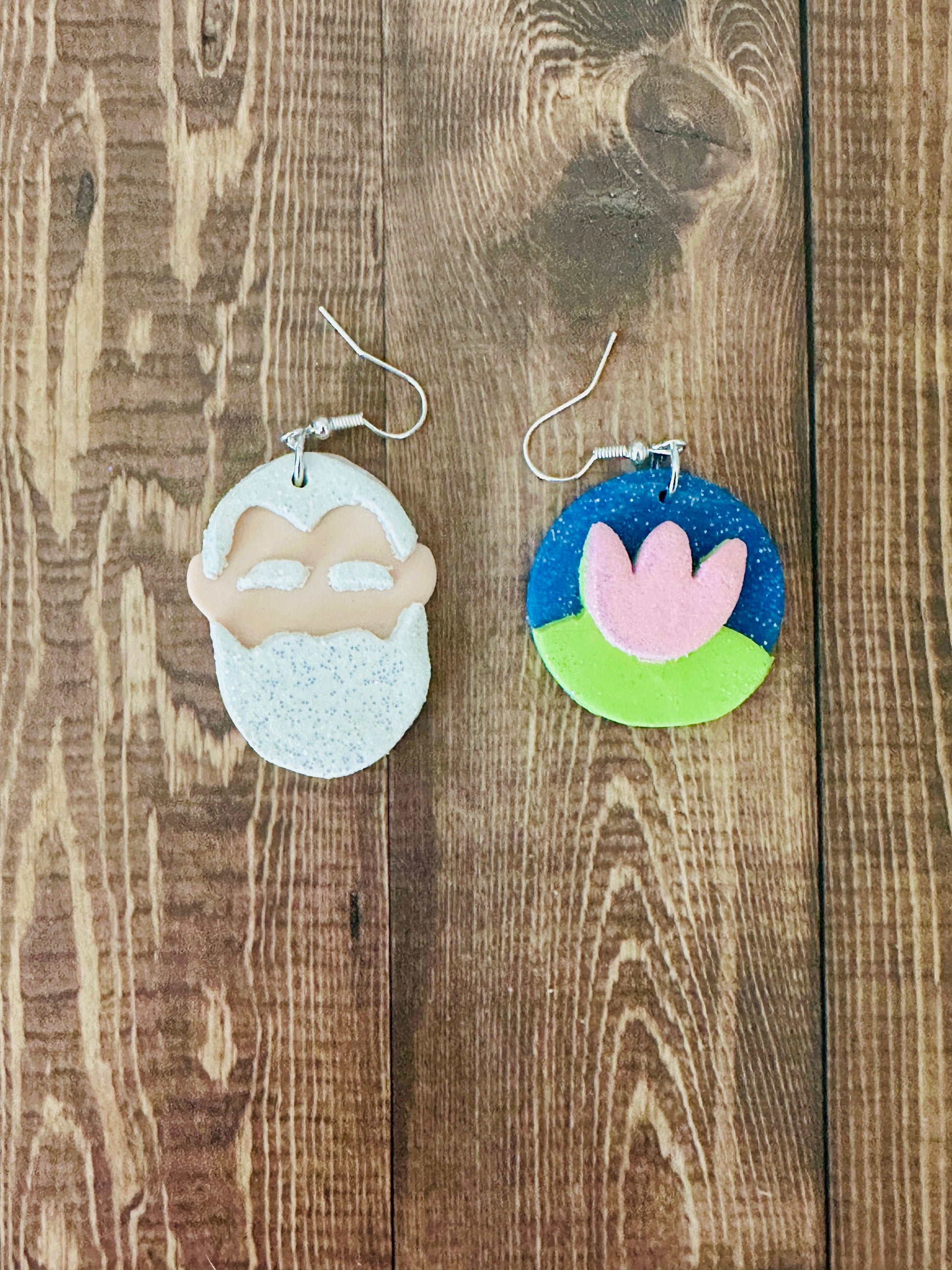 Handcrafted Claude Monet artist earrings with white beard portrait and water lily design on dark wooden table surface.