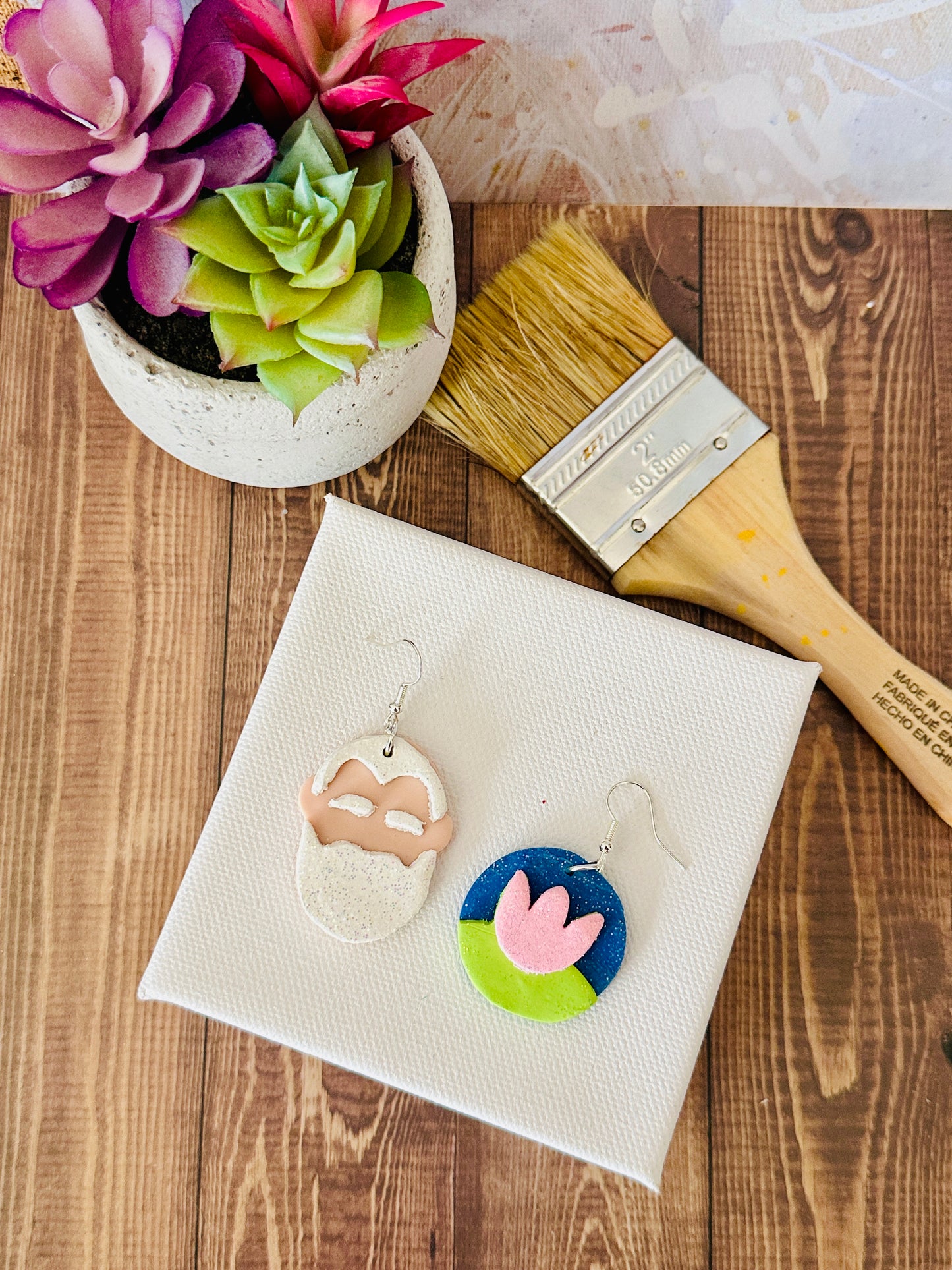 Lightweight art teacher earrings with Monet portrait and water lily flat on canvas with paintbrush and potted plants.