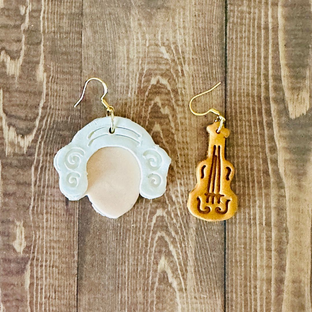 Two unique earrings, Mozart on left and Gold Violin on the right on a wooden background.