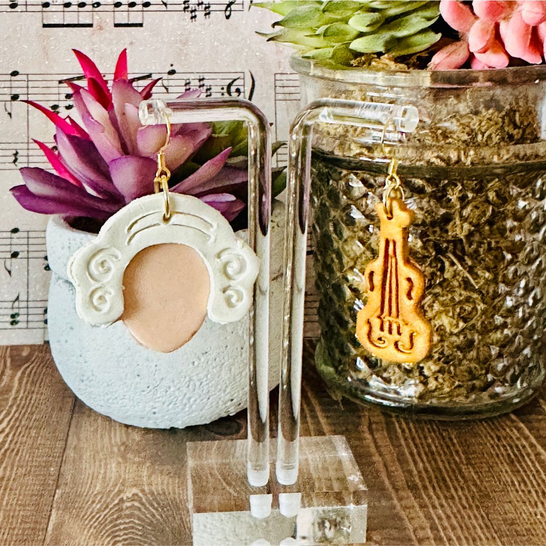 Mozart style earrings on stand with a decorative pot and plant in the background.