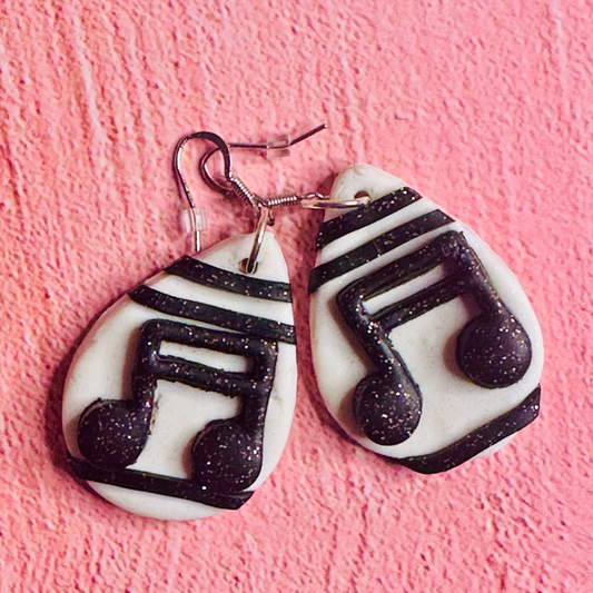A close up of the Musical Note Earrings on a pink background.  Each earring is white and shows connected eight notes on a music paper.
