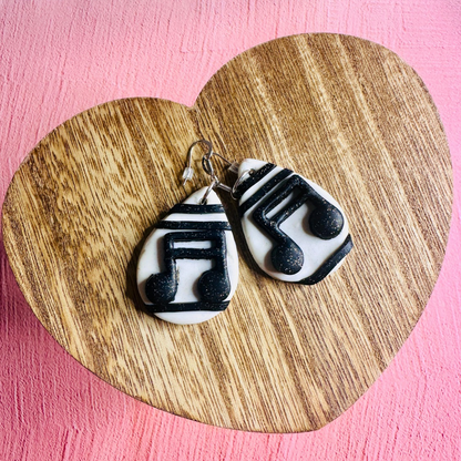 A set of musical note earrings on a wooden table shaped like a heart.