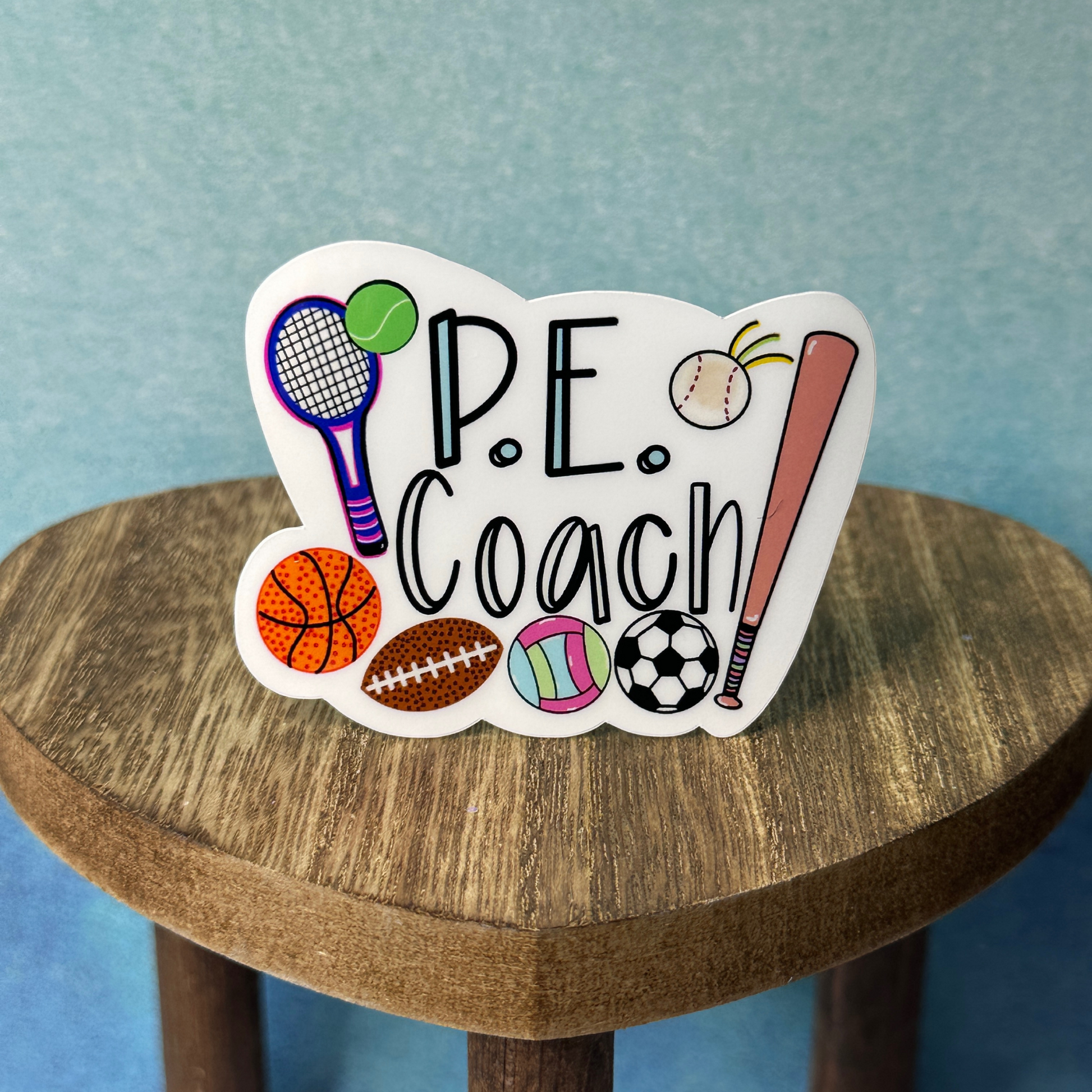 P.E. Coach waterproof vinyl sticker displayed on a wooden table in front of a blue wall.