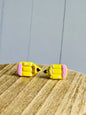 A set of pencil stud earrings on a wooden table  The stud is yellow with a pink eraser, white shadows, gold colored wood, and black pencil tip.
