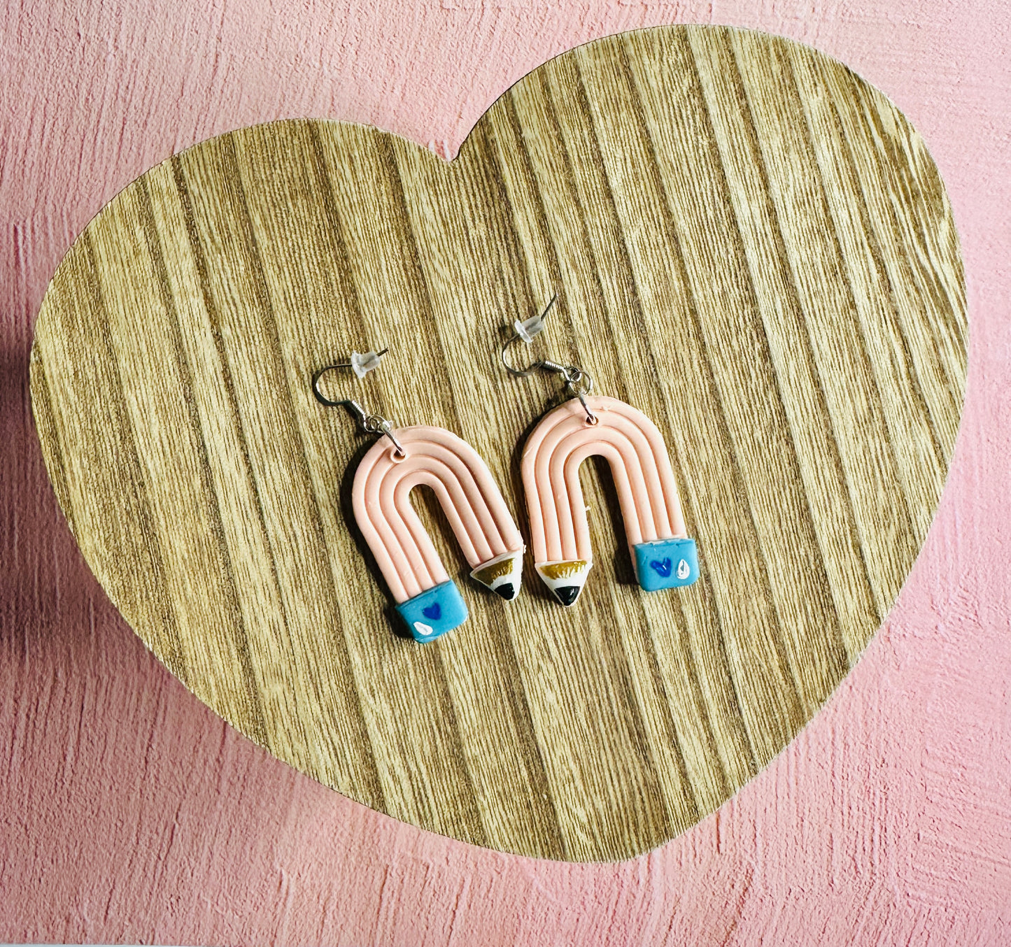 A wide view of the Pink Pencil Teacher Earrings.  The earrings are sitting on a table shaped like a heart.