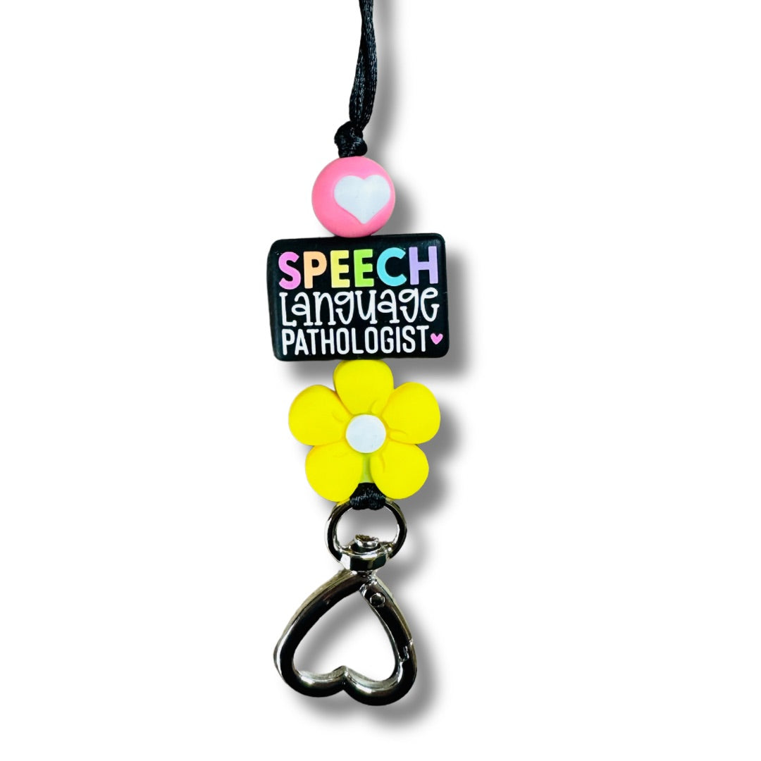 Close-up of speech language pathologist lanyard showing rainbow SPEECH focal bead, pink heart bead, yellow flower bead, and heart clasp on white background.