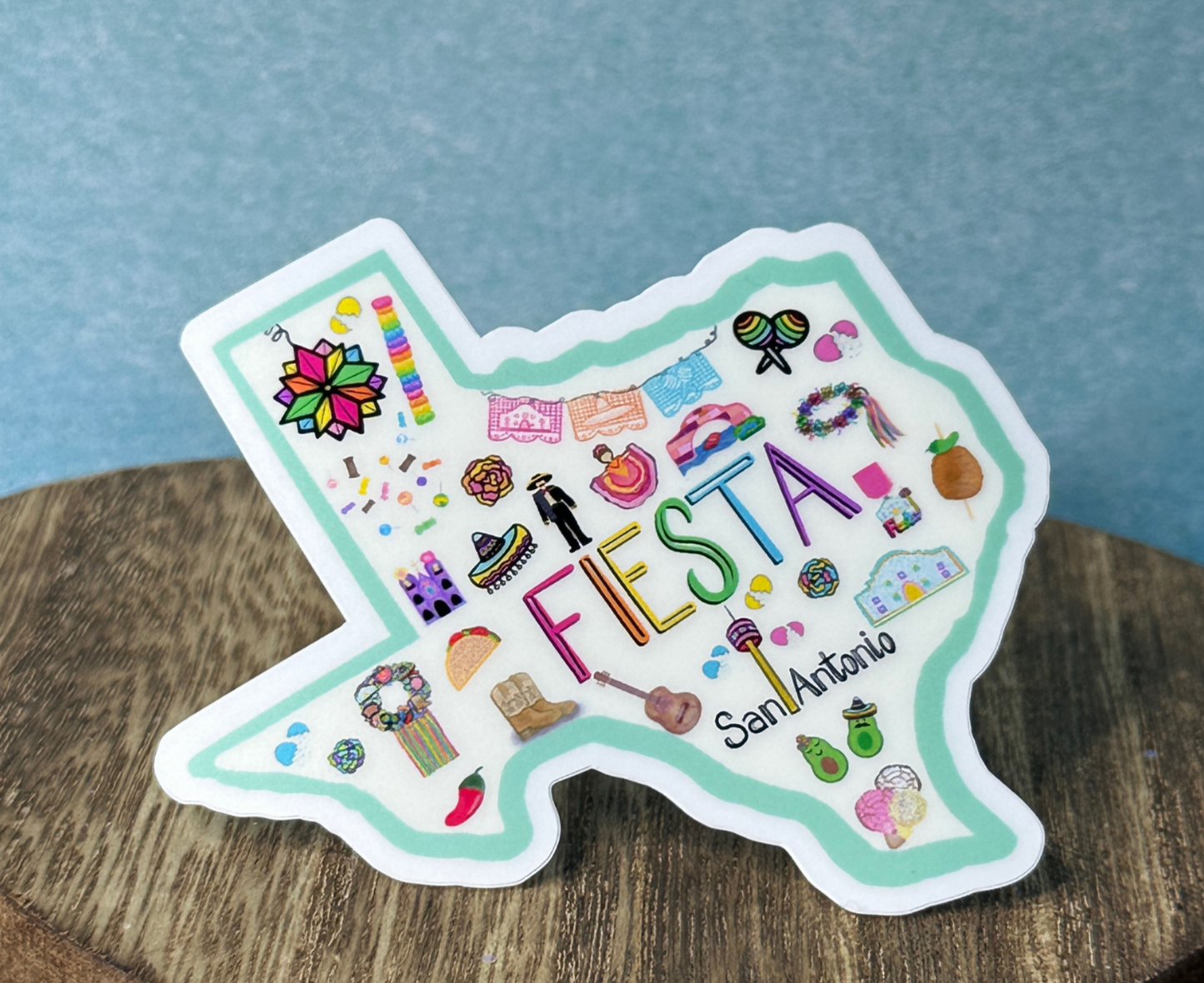 San Antonio Fiesta sticker on wooden table with blue background.  Texas Made.  Waterproof vinyl 2.5x2.4 inches
