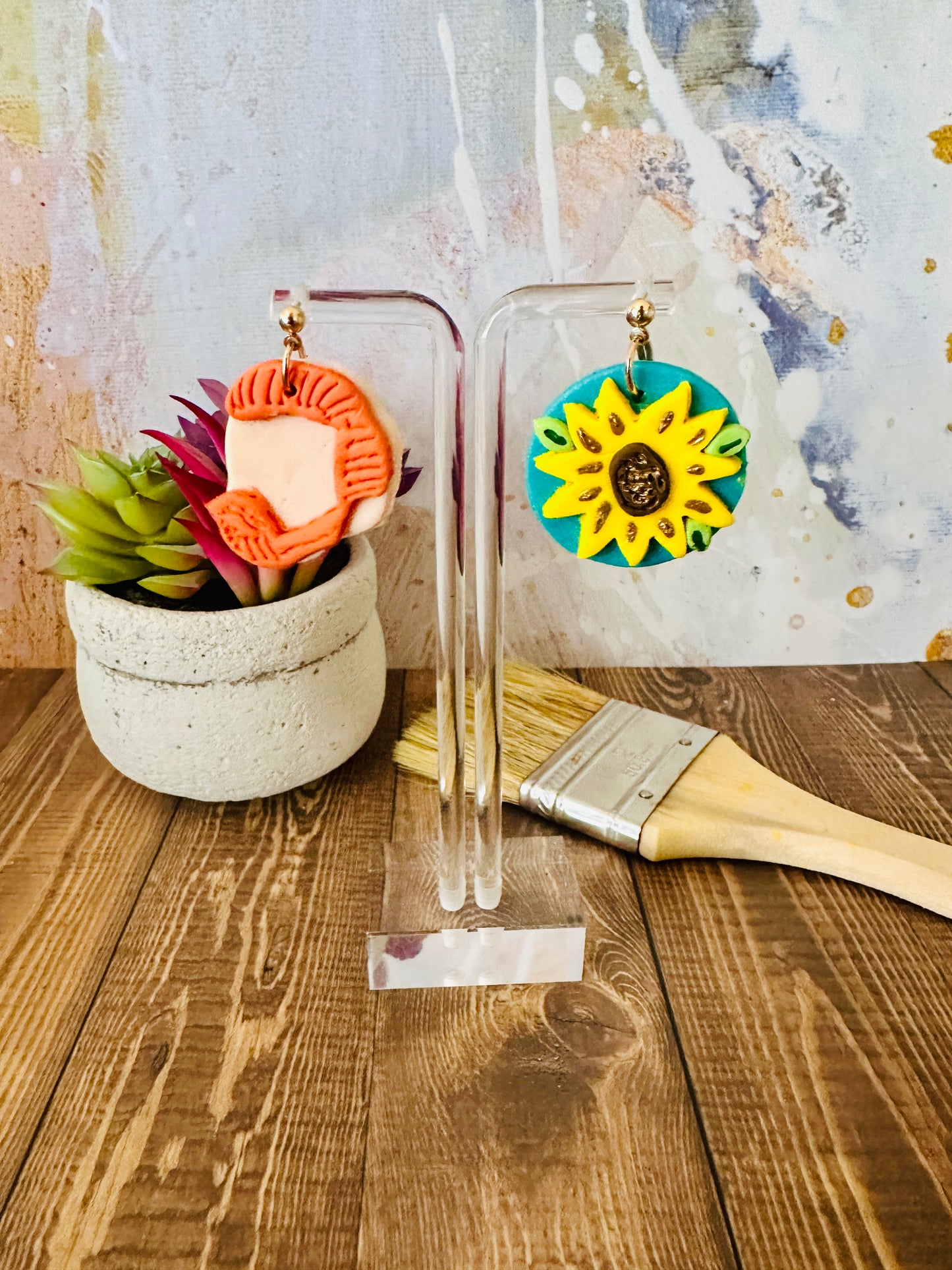 Lightweight polymer clay Van Gogh earrings small size on clear stand with plant, paintbrush, colorful abstract backdrop.