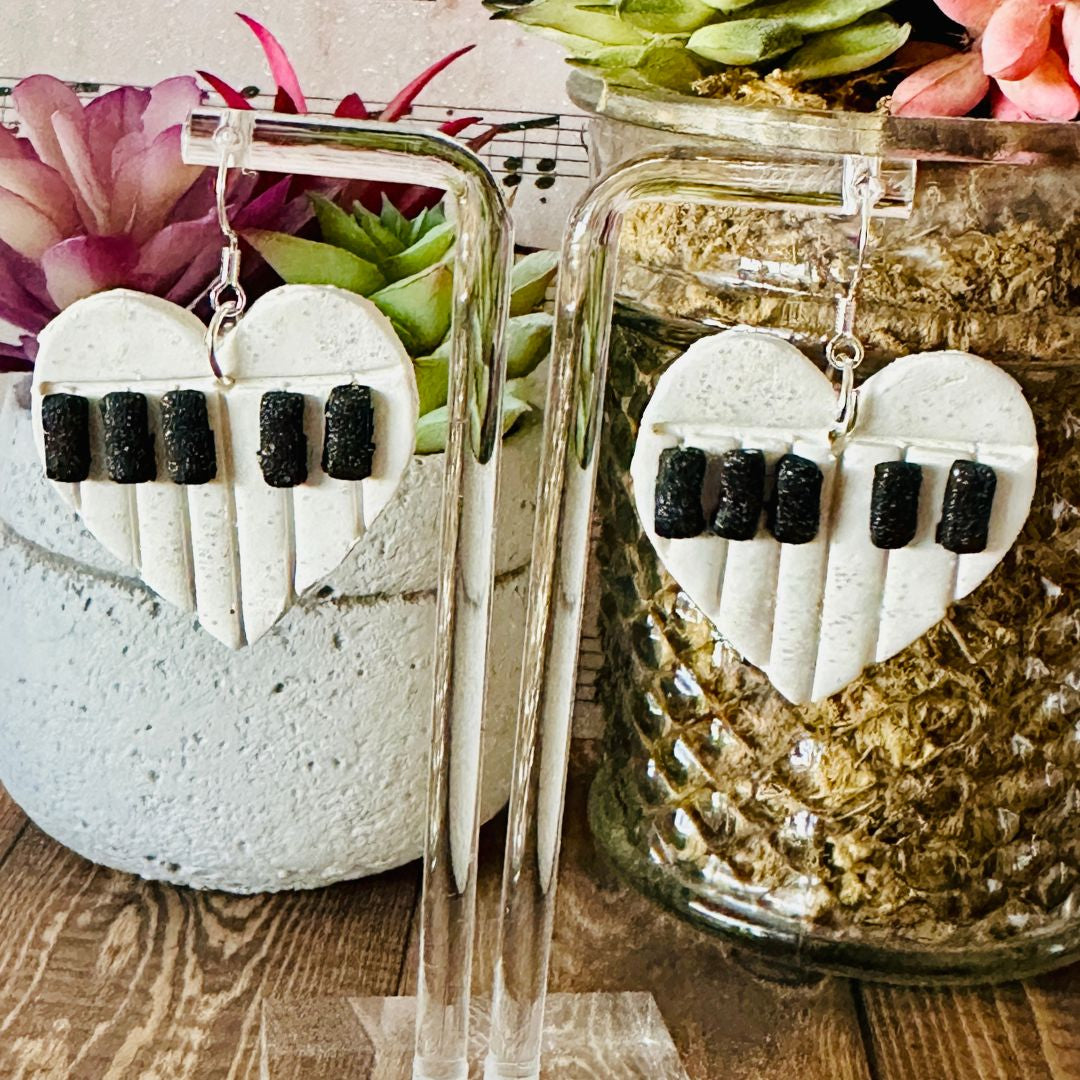Heart-shaped earrings with black and white design in front of a plant and decorative jars.