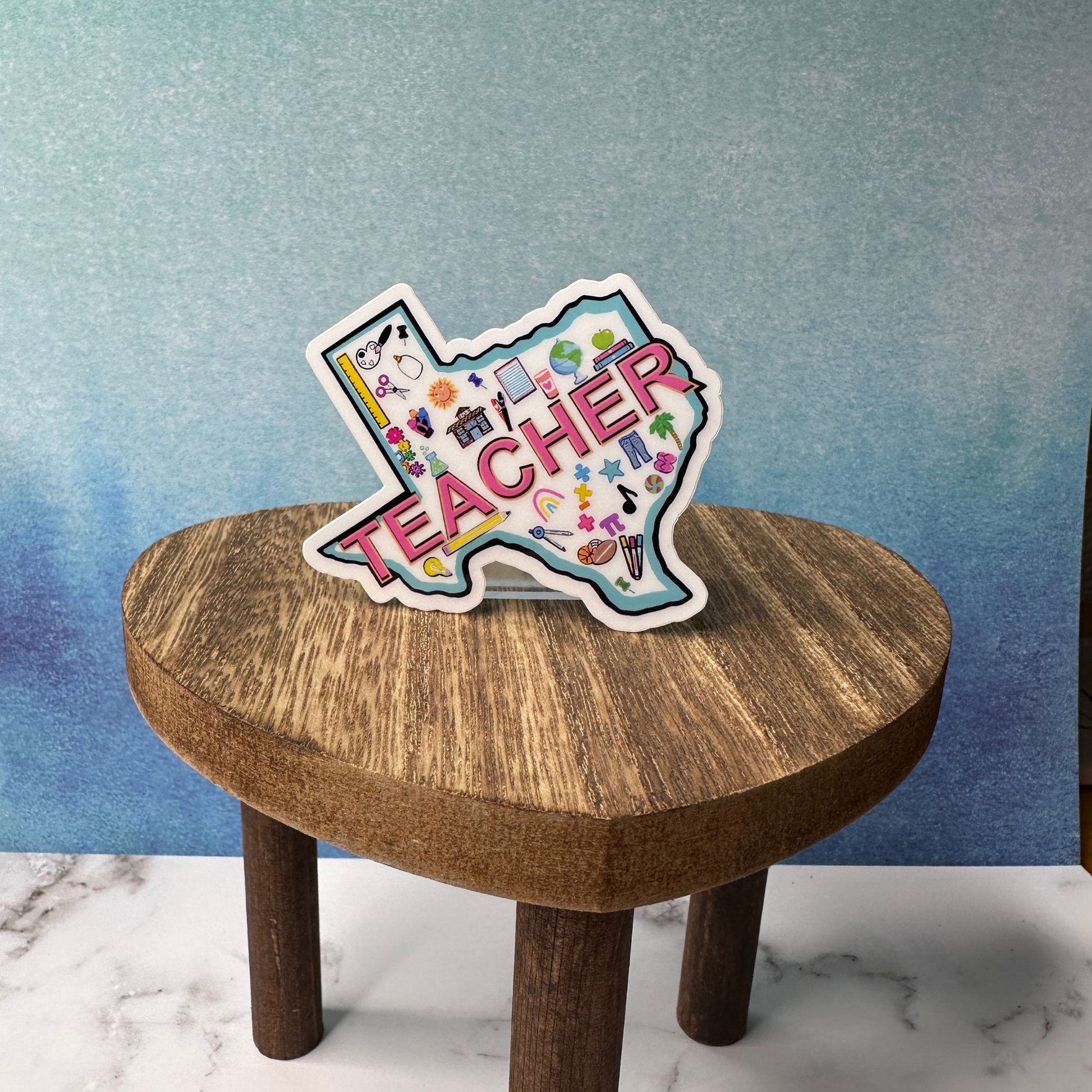 Texas Teacher waterproof vinyl sticker displayed on a wooden table in front of a blue wall,.