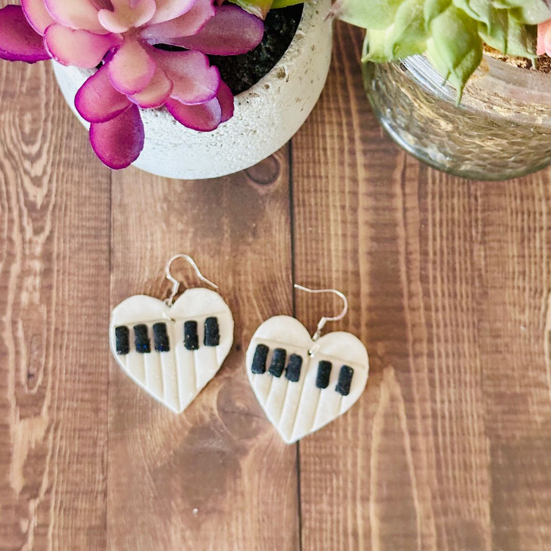 Heart-shaped earrings with piano key design on a wooden surface with plants.