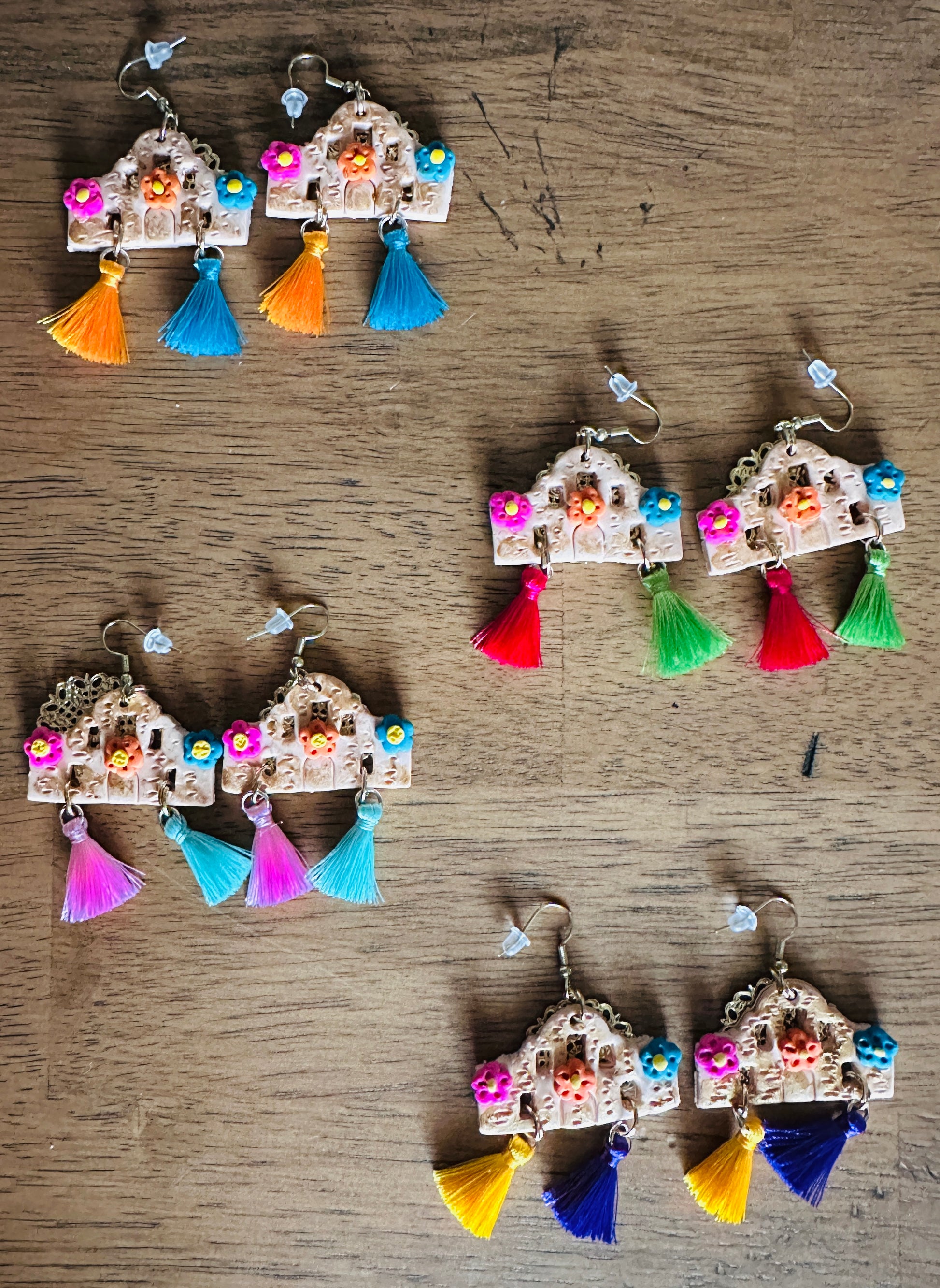 One pair of each color variant of the Alamo polymer clay earrings laying on a wooden table.