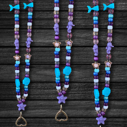 Three Under The Sea Mermaid Lanyards laying next to each other on a dark black wooden table.