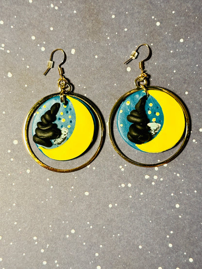 A pair of Van Gogh Starry Night earrings on a starry background.  The light and shadows look as if the sun is setting on the earrings.