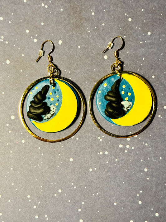 A pair of Van Gogh Starry Night earrings on a starry background.  The light and shadows look as if the sun is setting on the earrings.