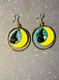 A pair of Van Gogh Starry Night earrings on a starry background.  The light and shadows look as if the sun is setting on the earrings.