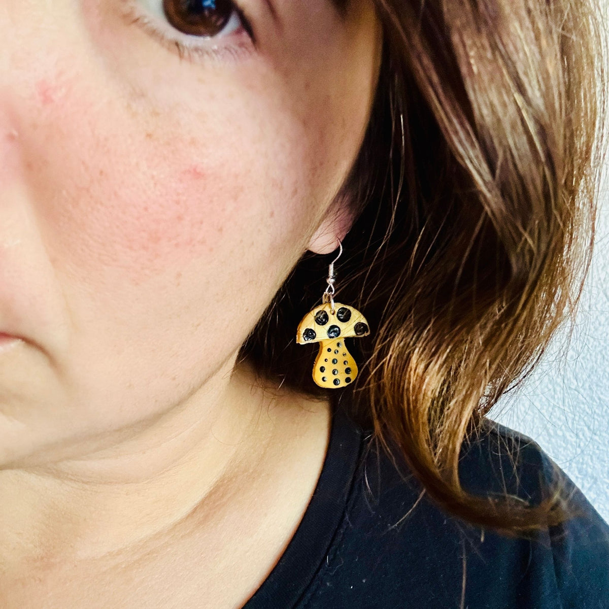 Woman wearing Yayoi Kusama inspired polymer clay earrings showing yellow mushroom with black polka dots, perfect statement jewelry for artists.