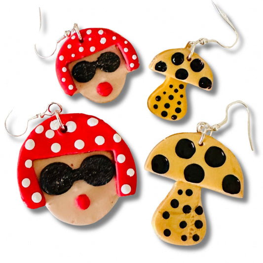 Size comparison of Yayoi Kusama polymer clay earrings showing large and small variants with portrait, red polka dot hair, and yellow mushroom on white background.