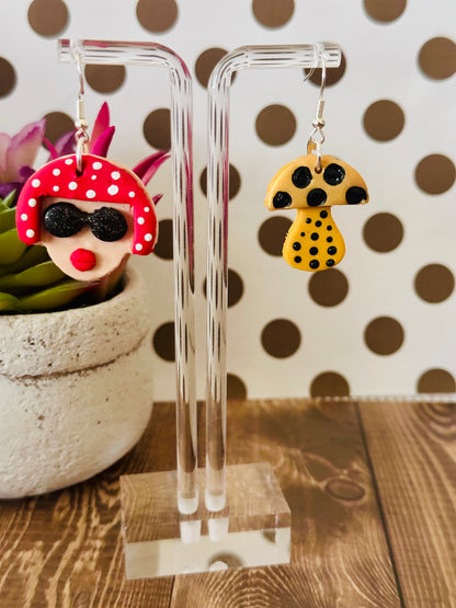 Close-up of Yayoi Kusama polymer clay earrings on clear stand with polka dot background and wooden table, highlighting handcrafted details.