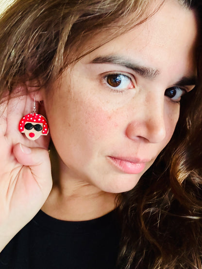 Woman wearing Yayoi Kusama polymer clay earrings displaying the portrait earring with red polka dot hair, black sunglasses and red lips.