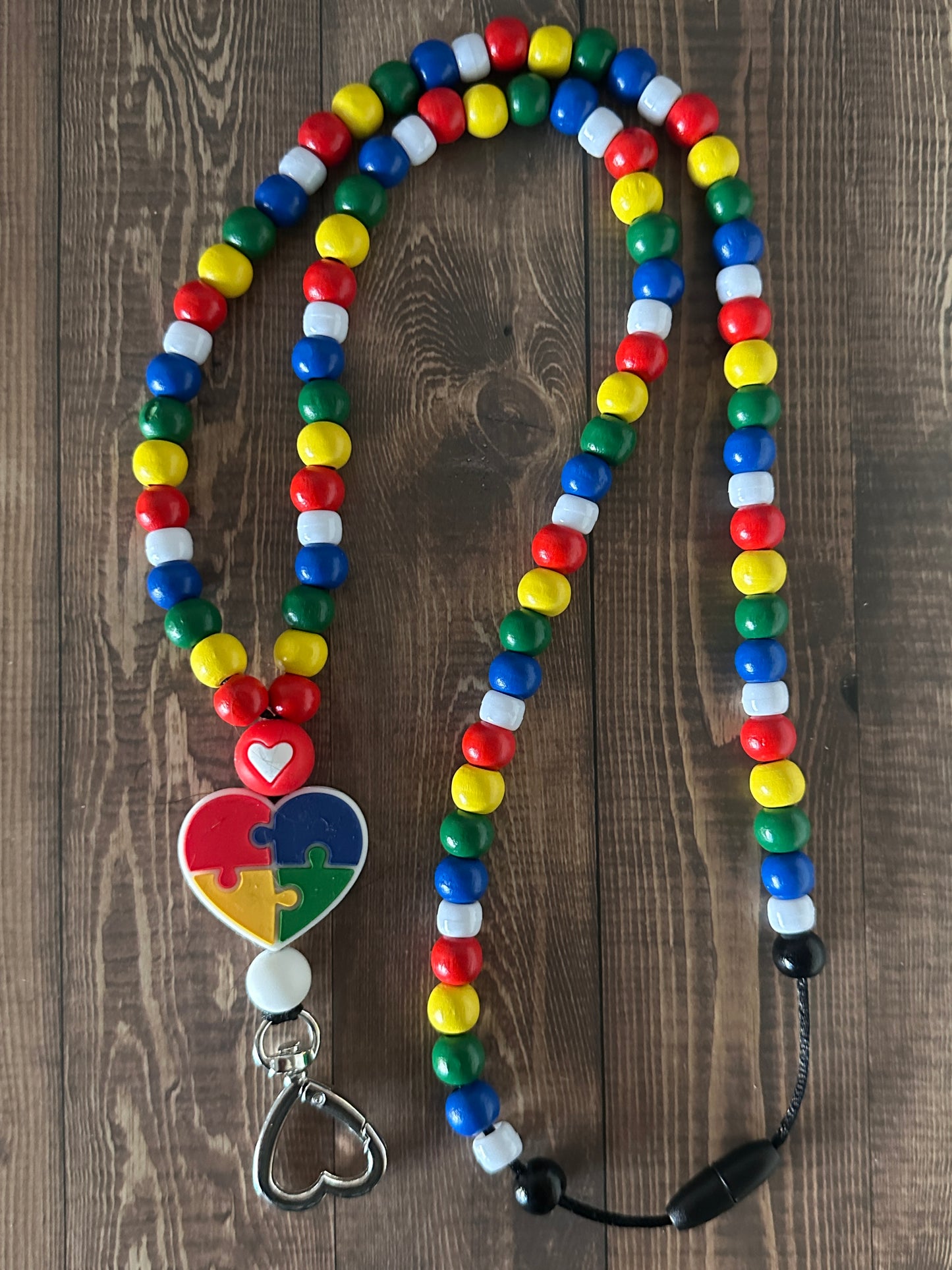 Puzzle Heart Autism Awareness Lanyard with rainbow wooden beaded version displayed on a wooden table.