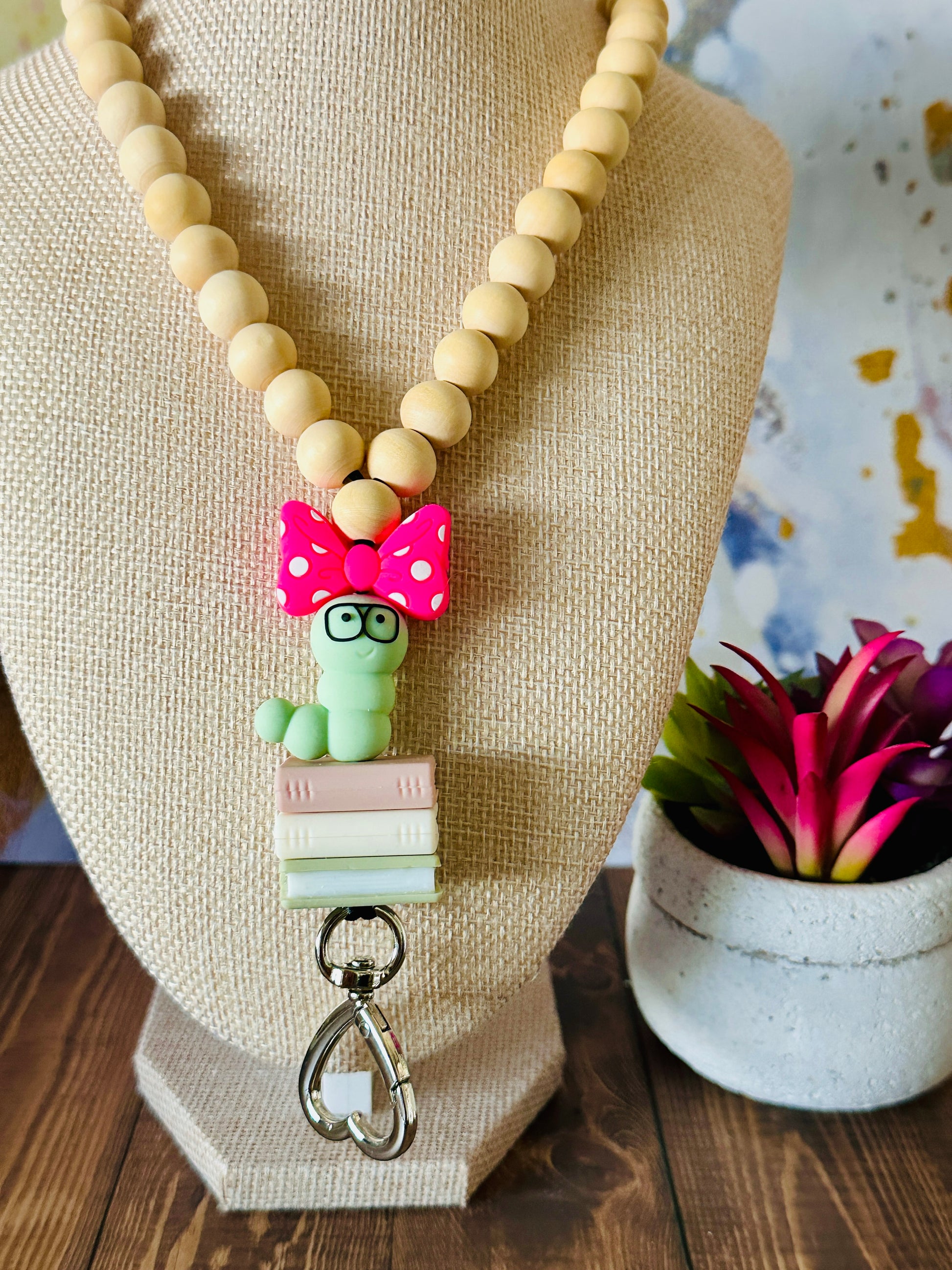 Front view of bookworm wooden bead lanyard on mannequin with a potted succulent in the background.