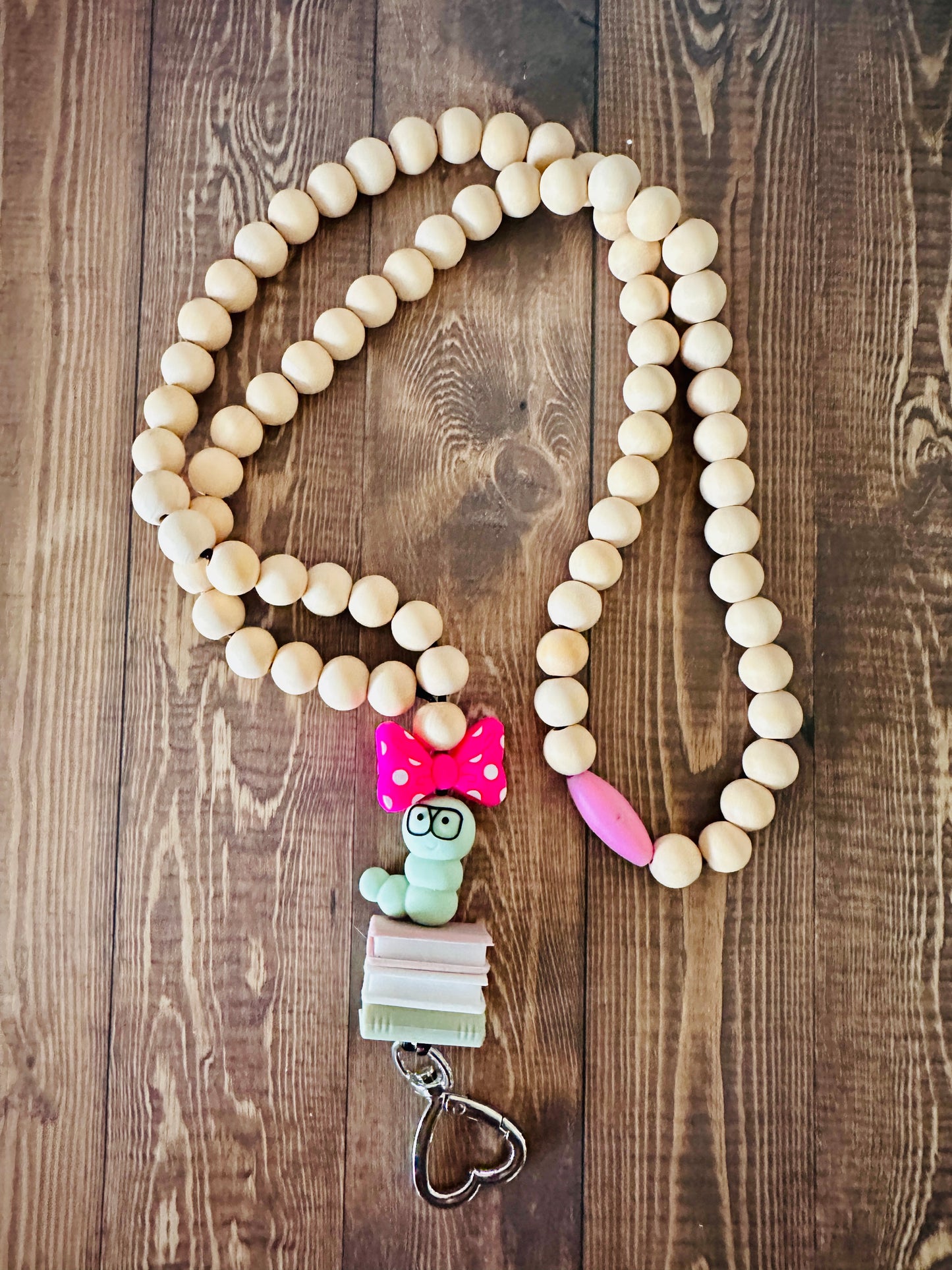 Full view of handmade bookworm wooden bead teacher lanyard laid flat on a wooden table.