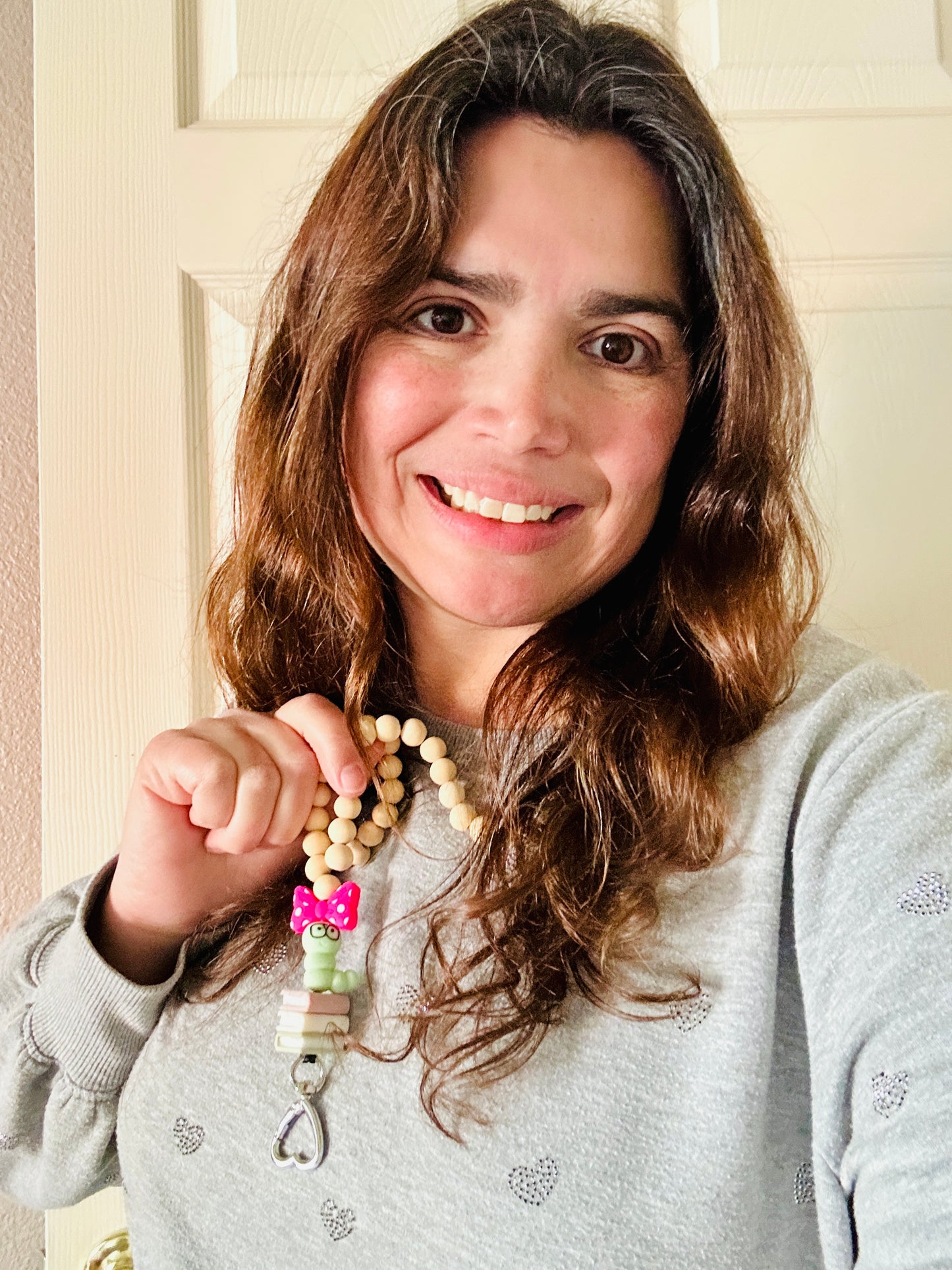 Woman wearing handmade bookworm lanyard and holding up the bookworm focal bead with black glasses and pink bow.