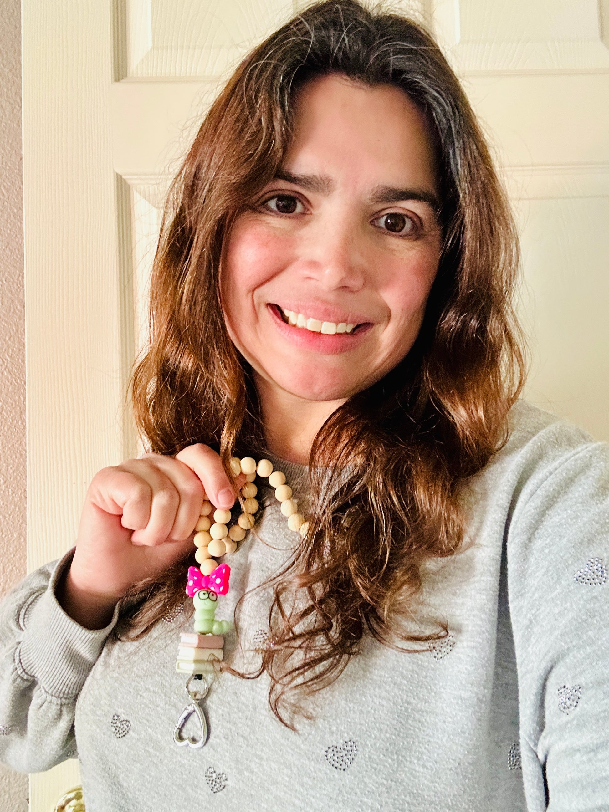 Woman wearing handmade bookworm lanyard and holding up the bookworm focal bead with black glasses and pink bow.