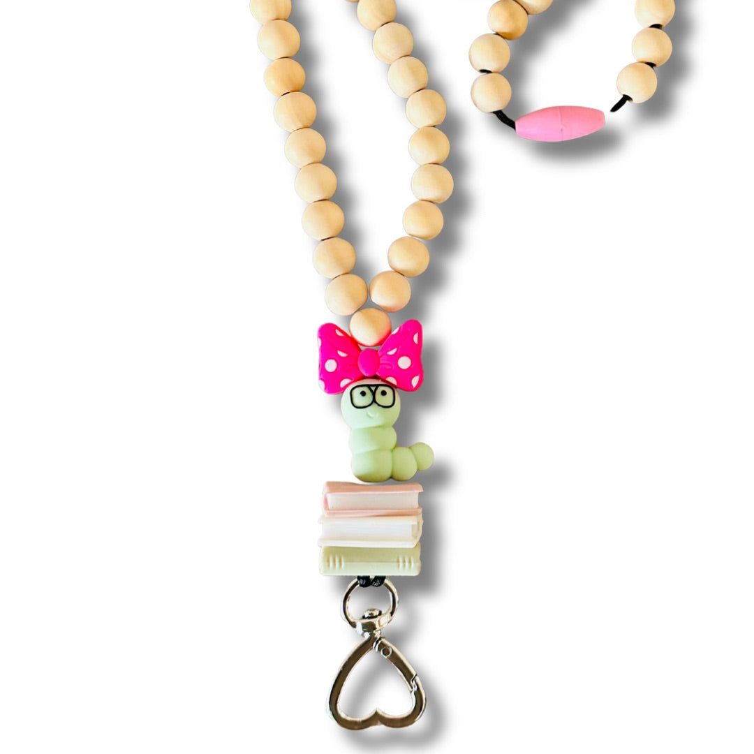 Close-up of bookworm focal bead with black glasses and pink bow, heart-shaped clasp, and wooden beads on lanyard.
