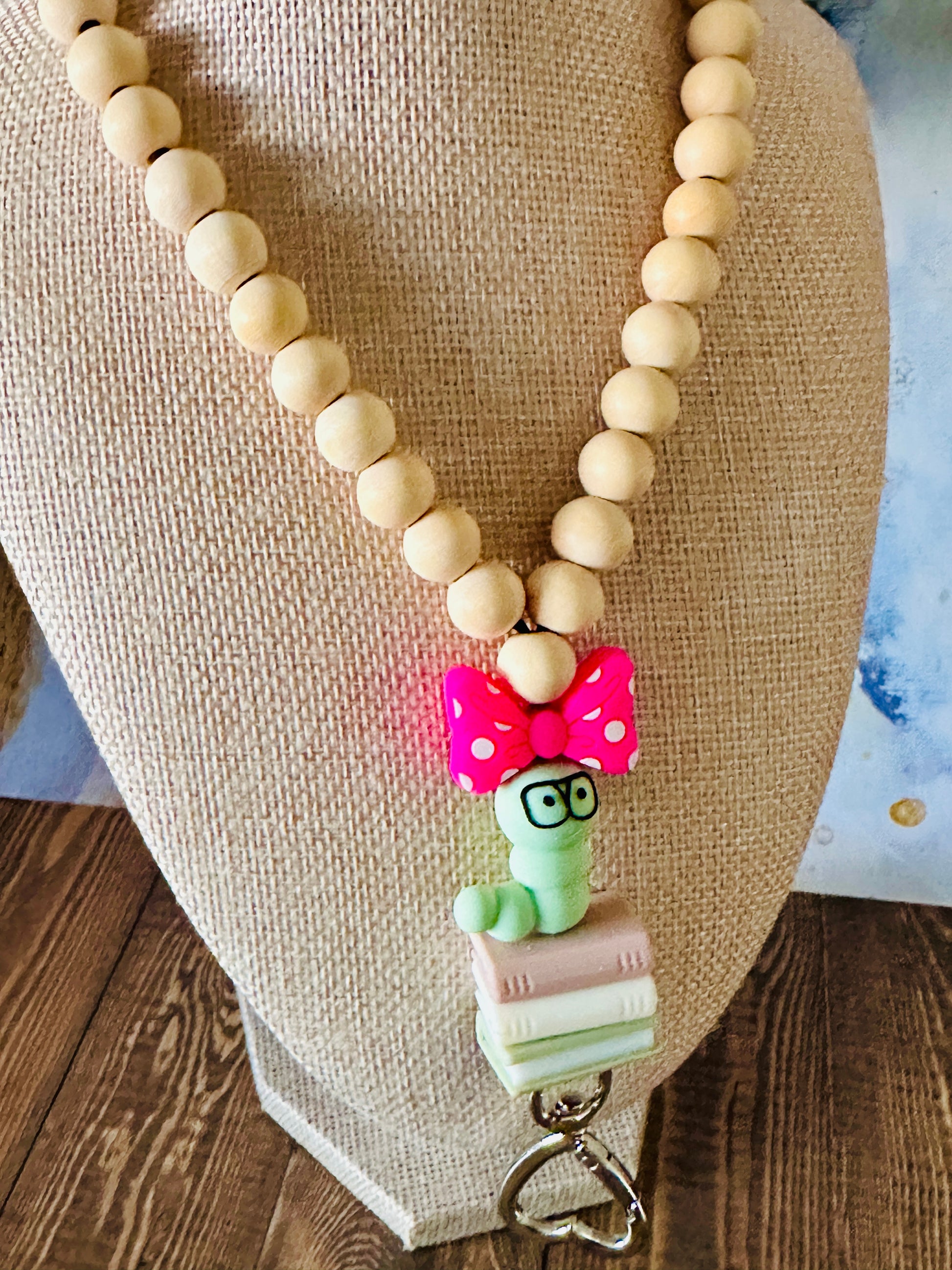 Angled view of handmade bookworm lanyard with wooden beads on a mannequin displayed on a wooden table.