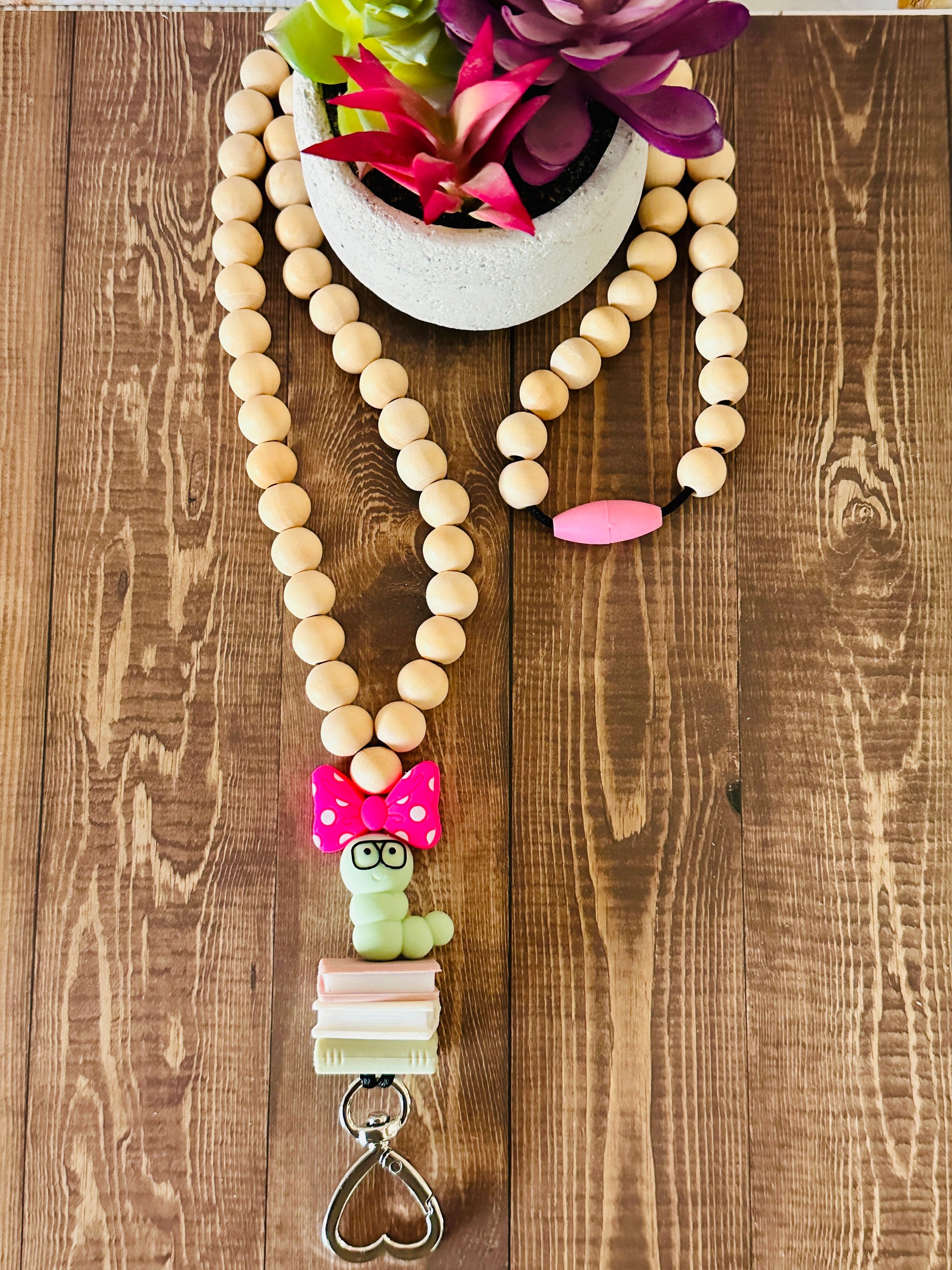 Handmade bookworm lanyard with wooden beads laid flat on a wooden table wrapped around a small potted succulen