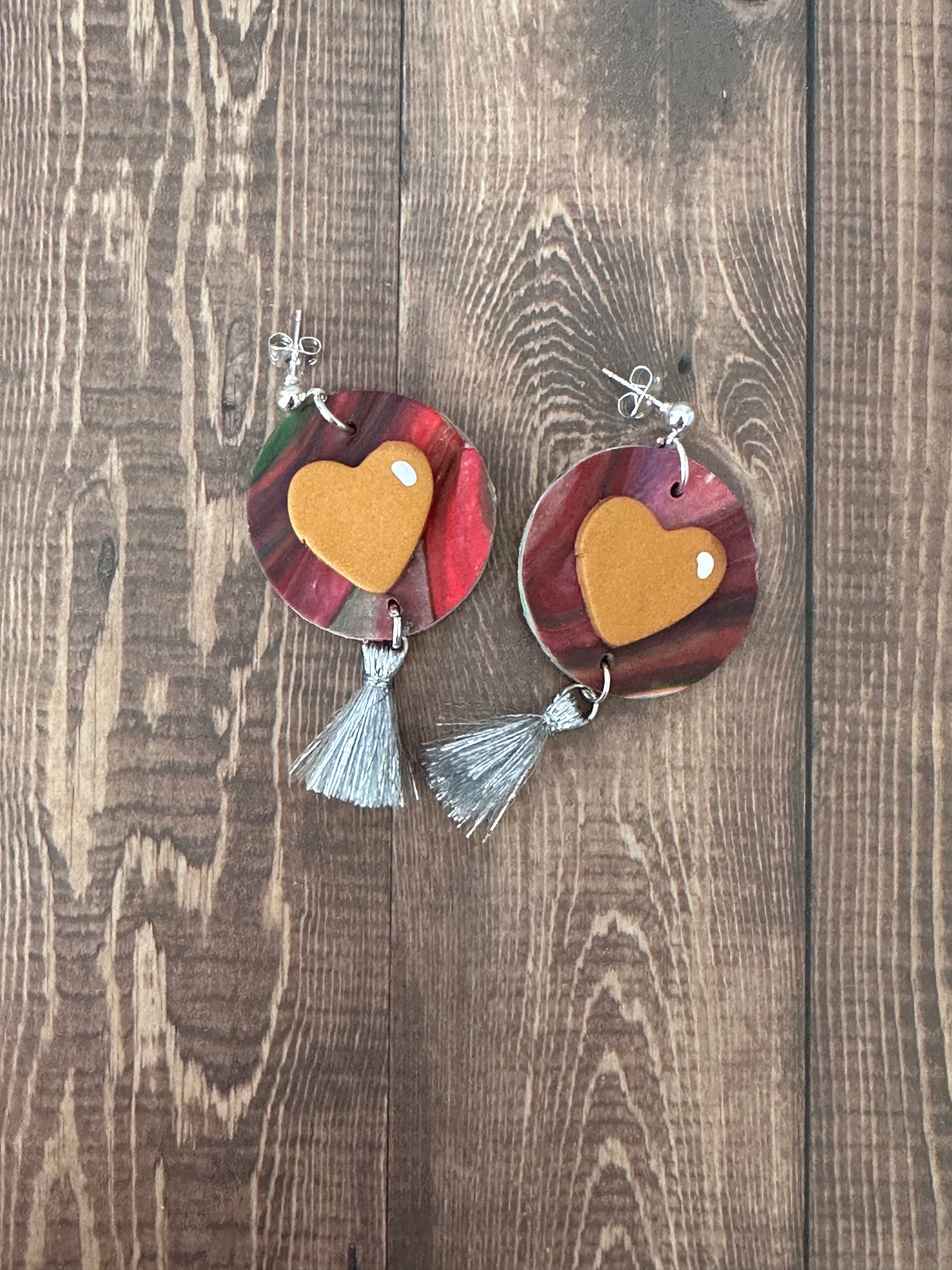 Flat lay of Jim Dine-inspired polymer clay earrings with silver tassel on a dark wooden table.