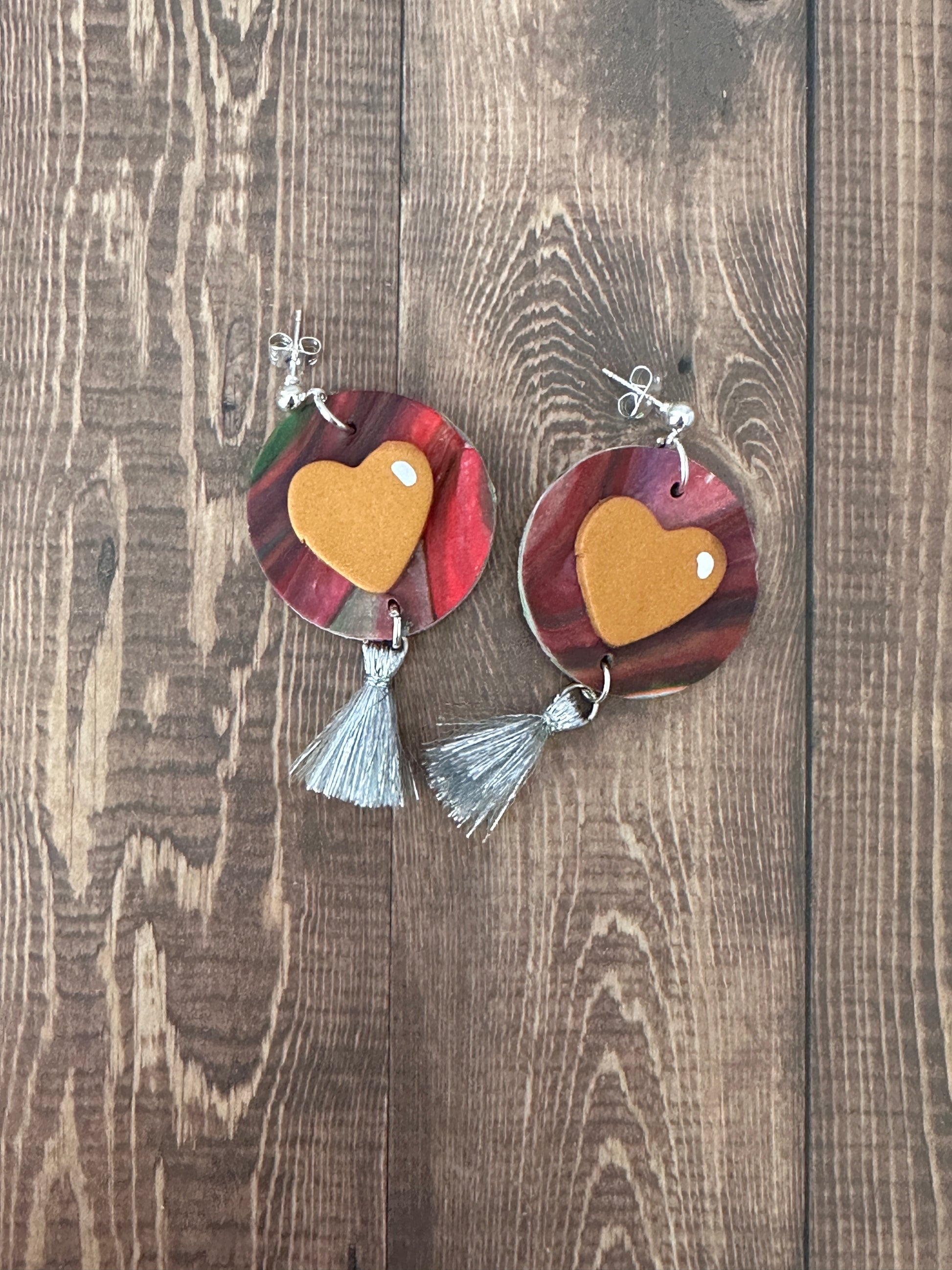 Flat lay of Jim Dine-inspired polymer clay earrings with silver tassel on a dark wooden table.