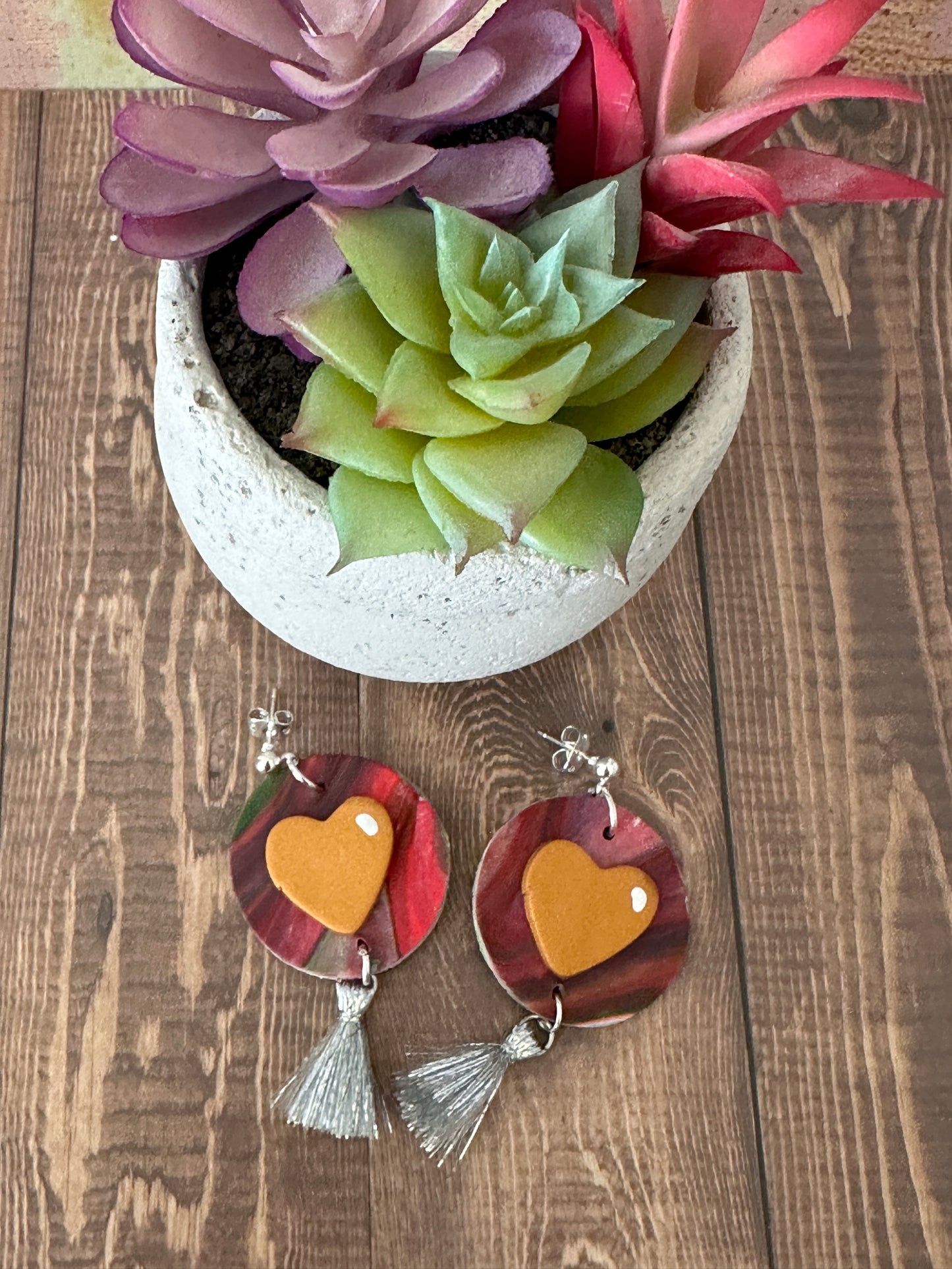 Abstract red pink and grey polymer clay earrings with orange heart beside a potted succulent