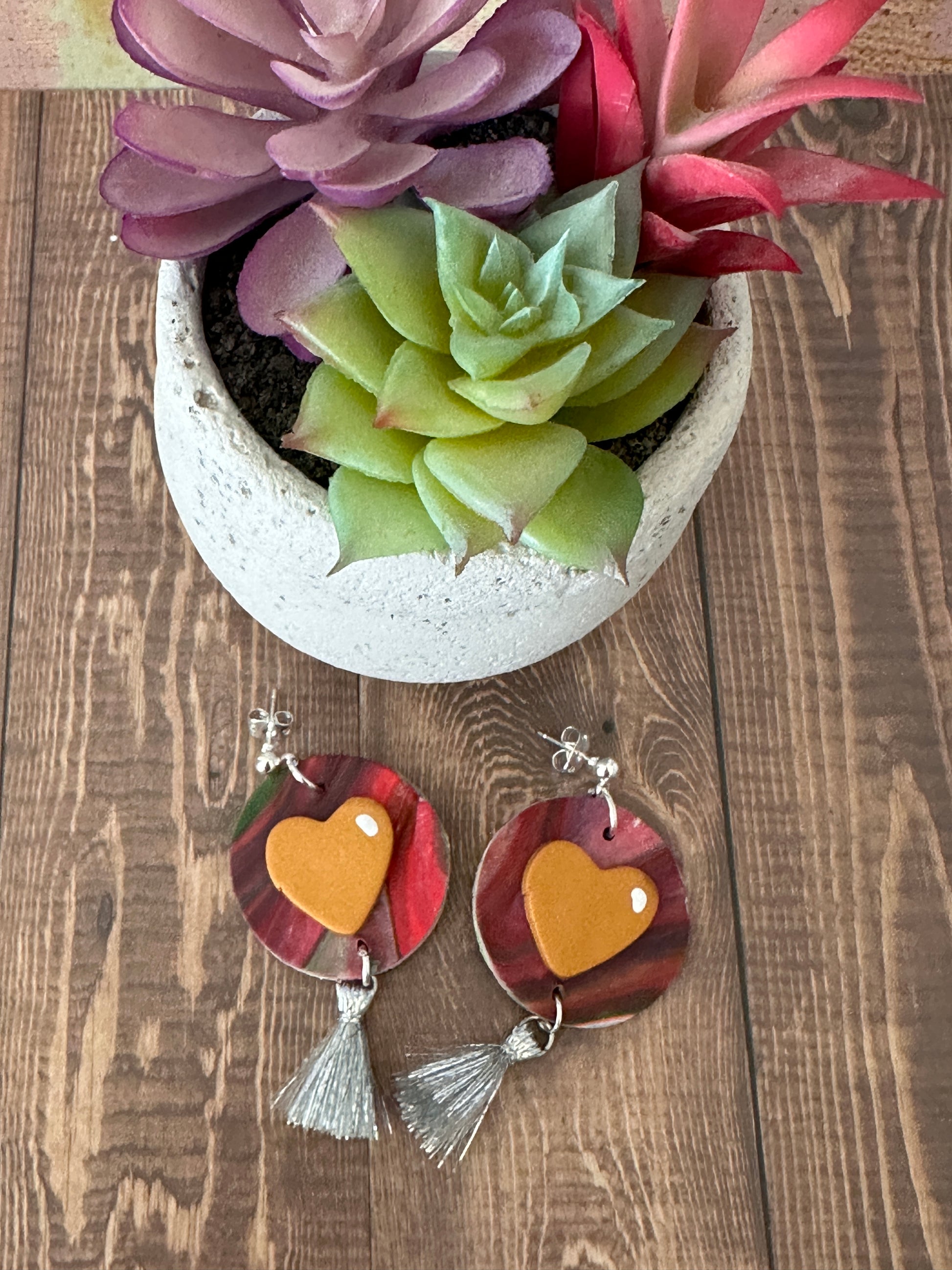 Abstract red pink and grey polymer clay earrings with orange heart beside a potted succulent