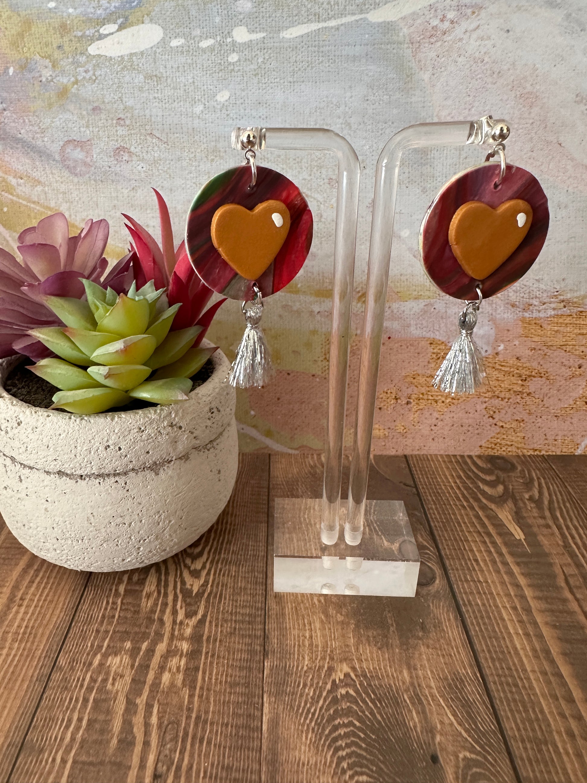 Jim Dine heart-inspired earrings on a display stand next to a potted plant, handmade in Texas.
